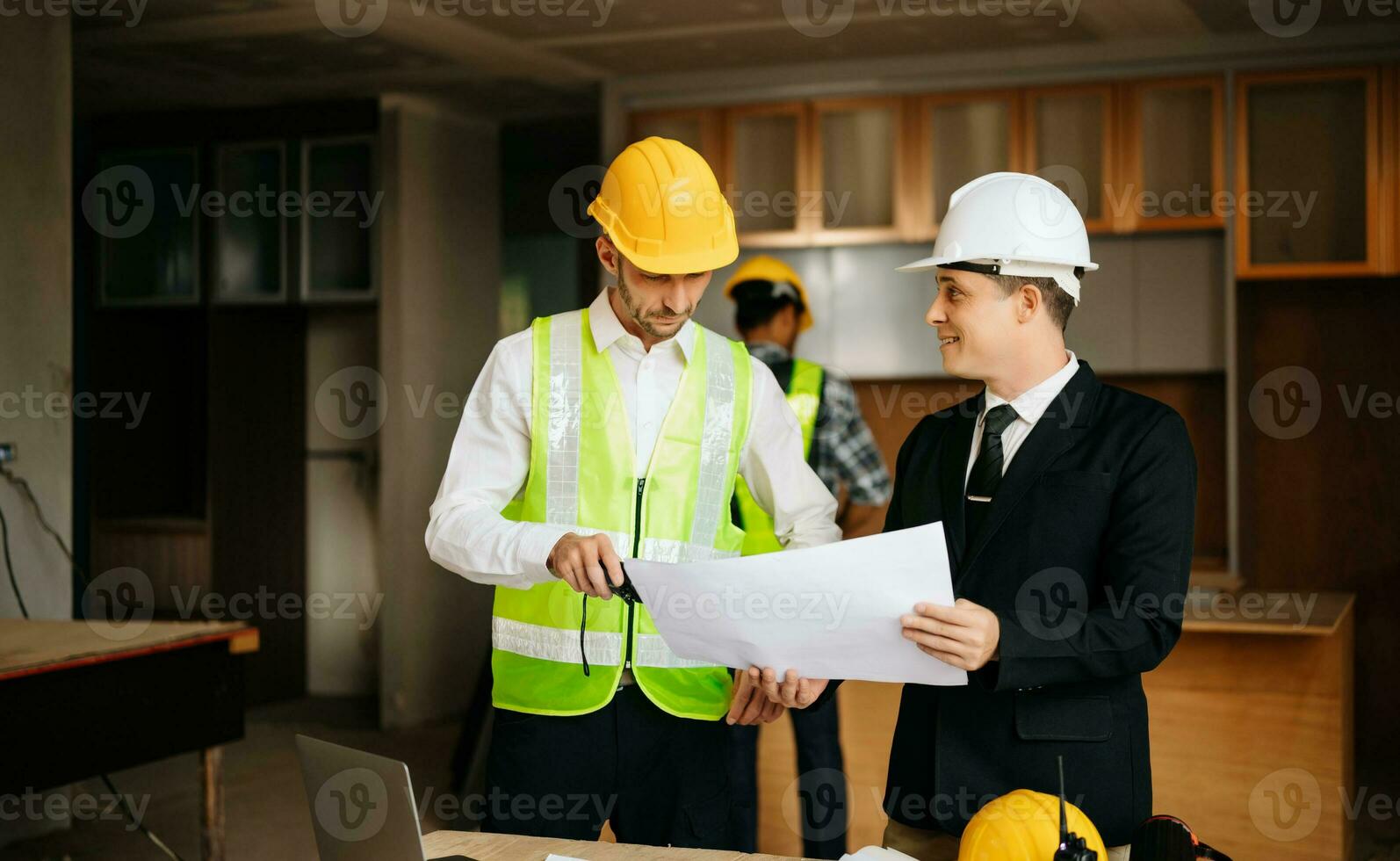 Contractor and architect looking at plan, tablet, laptop and talking about working on big project. Building in construction interior. photo