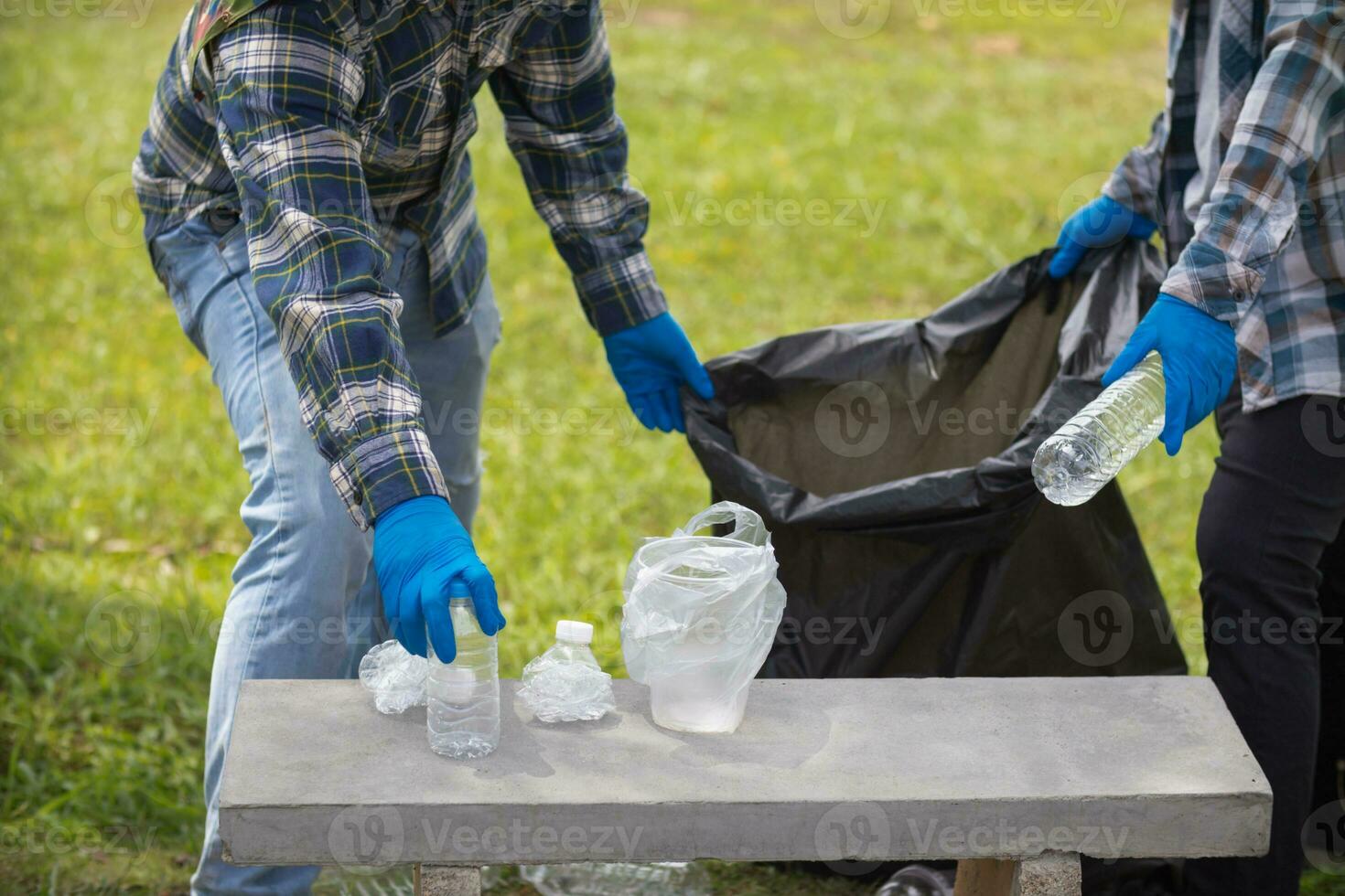 Two man employees use black garbage bags to collect plastic bottles and recyclable waste from the lawn and sidewalks for recycling. Concept of sorting plastic waste for recycling photo