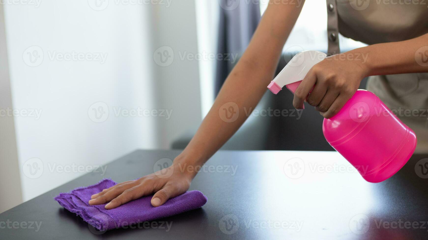 Cleaning staff is wiping cloth with cleaner and disinfectant on the surface of table to make the table clean with cleaning products and free from germs clinging to surface of the table in living room. photo