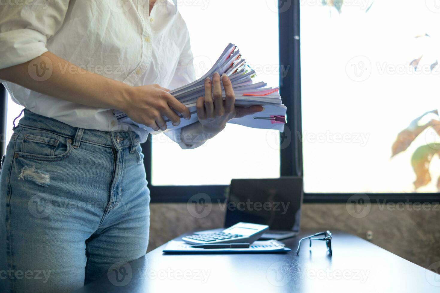secretary searches through stacked paperwork on desk in office to find lease within stacked paperwork just before meeting. concept difficulty in finding hire purchase contract from stacked paperwork photo