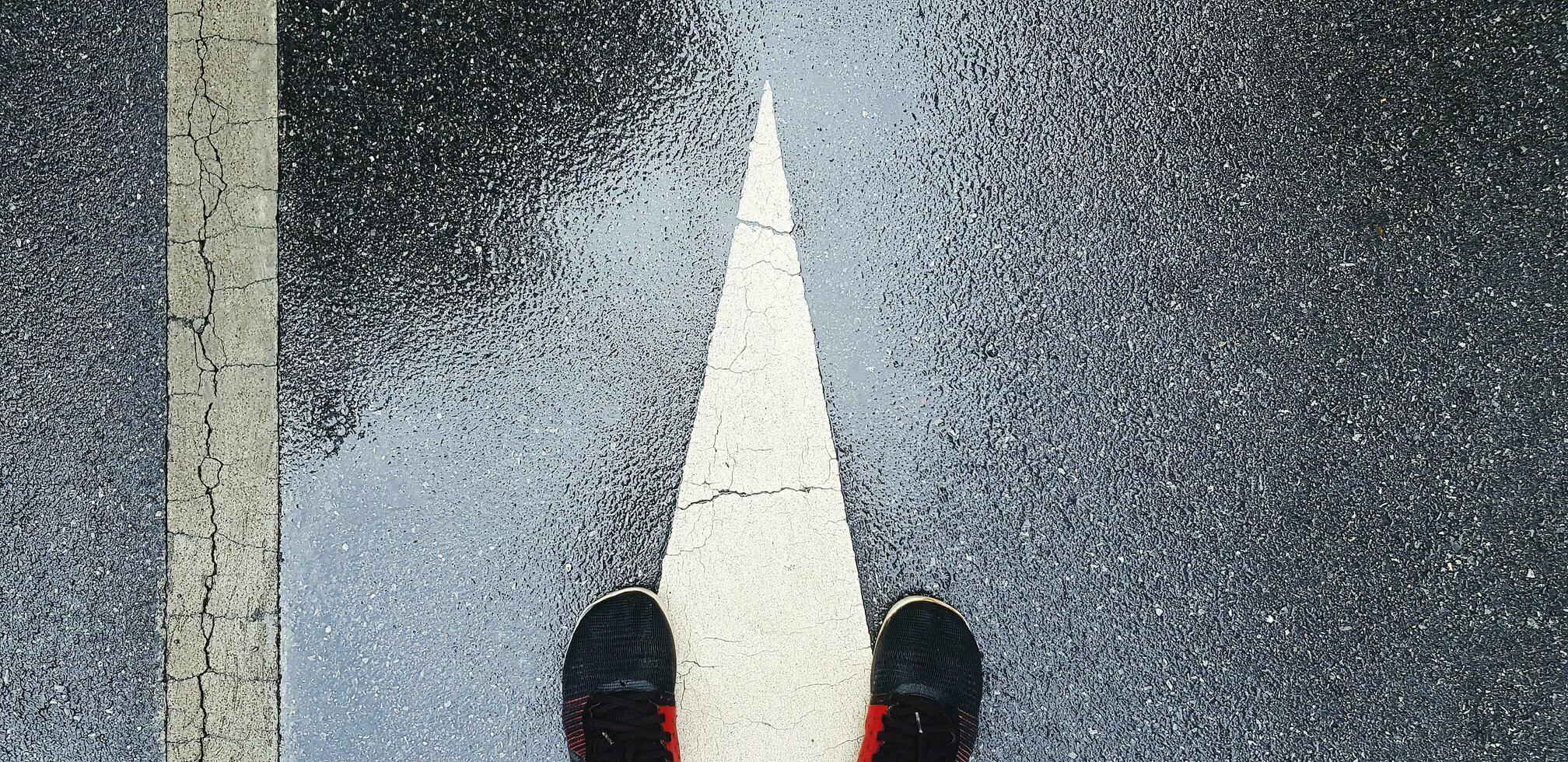 parte superior ver o plano laico de zapatilla de deporte o corriendo Zapatos en mojado calle o la carretera con blanco final de dirección firmar y línea con Copiar espacio. bromas y ejercicio después lloviendo. foto