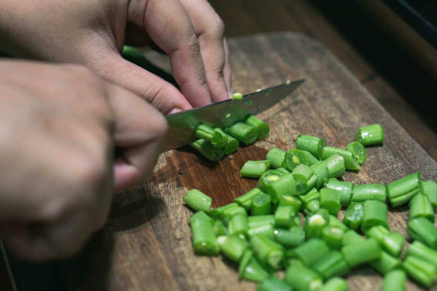 Photo of female hand chopping green beans on wooden cutting board for cooking