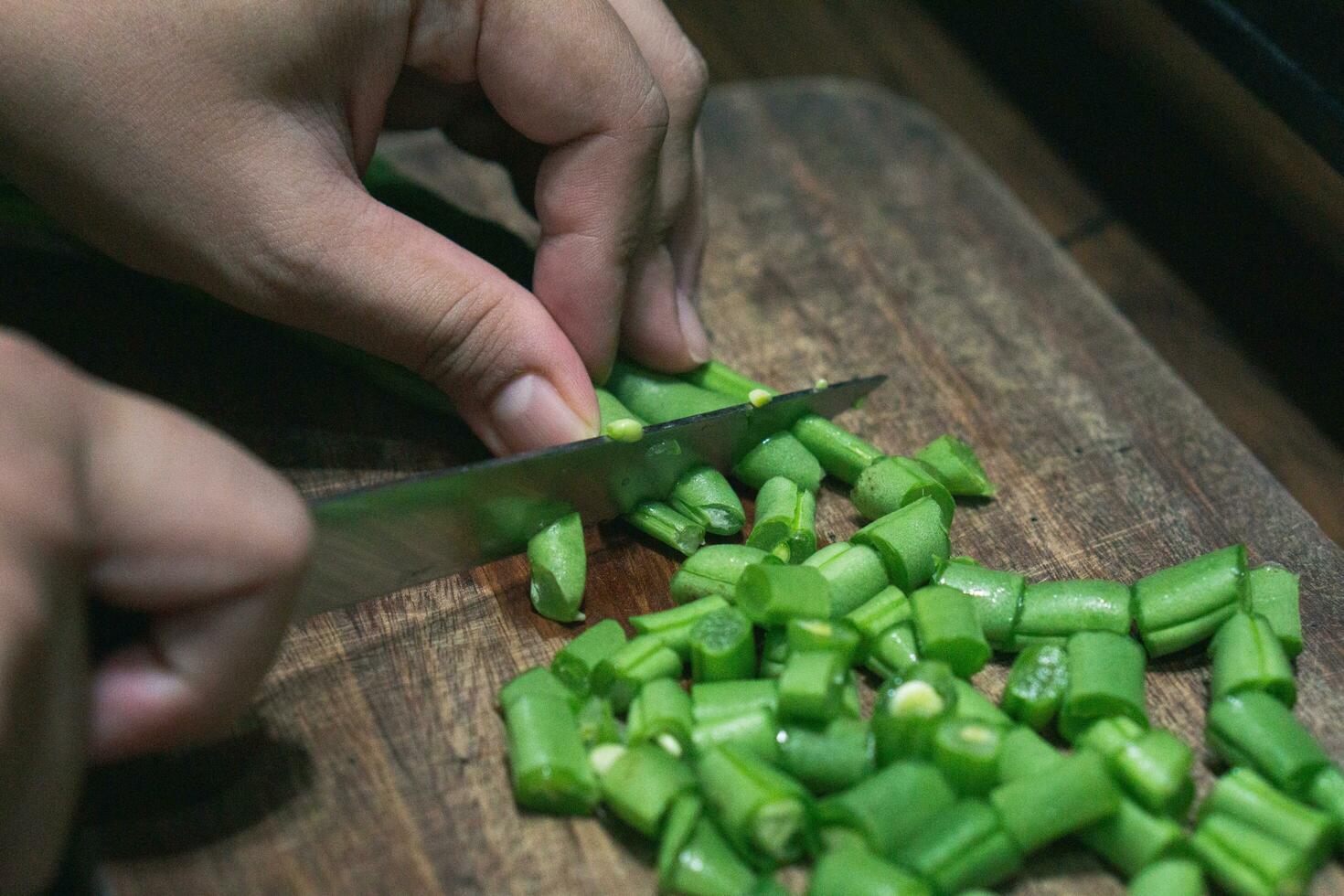 Photo of female hand chopping green beans on wooden cutting board for cooking