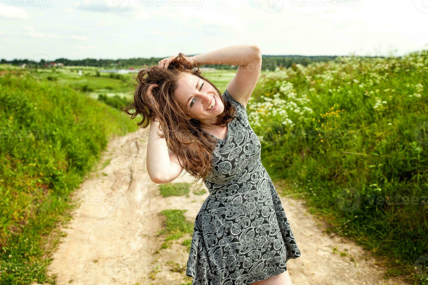 Beauty Girl Outdoors enjoying nature. Beautiful woman jumping on summer Field with blooming wild flowers, Sun Light. Free Happy Woman. photo