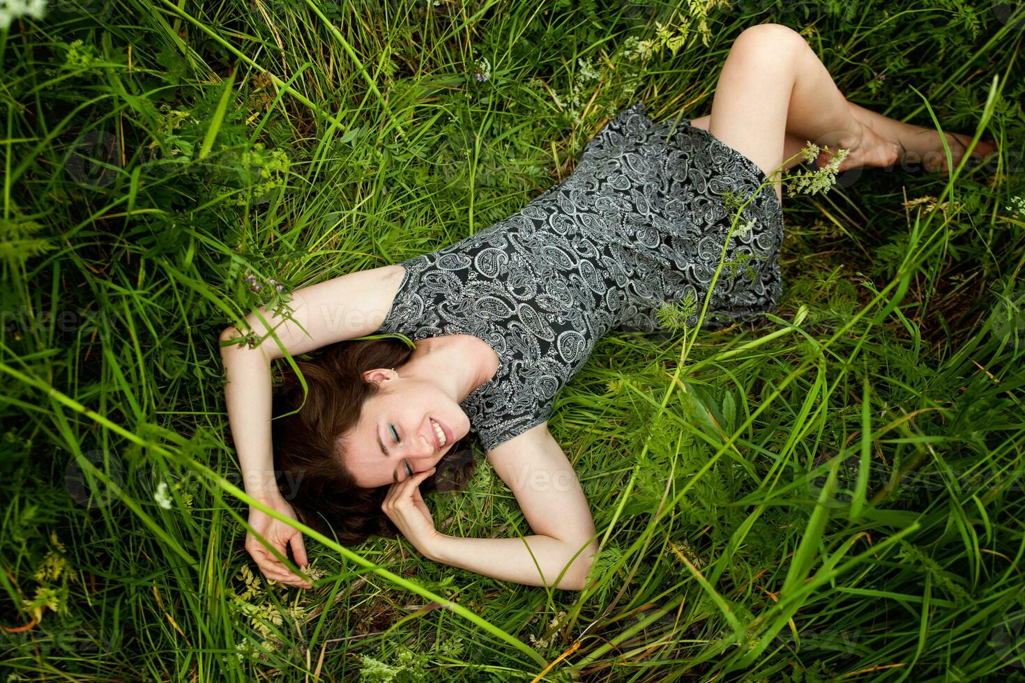 Brunette woman lying on green grass. Beauty Girl Outdoors enjoying nature and relaxation. Free Happy Woman, Top view photo