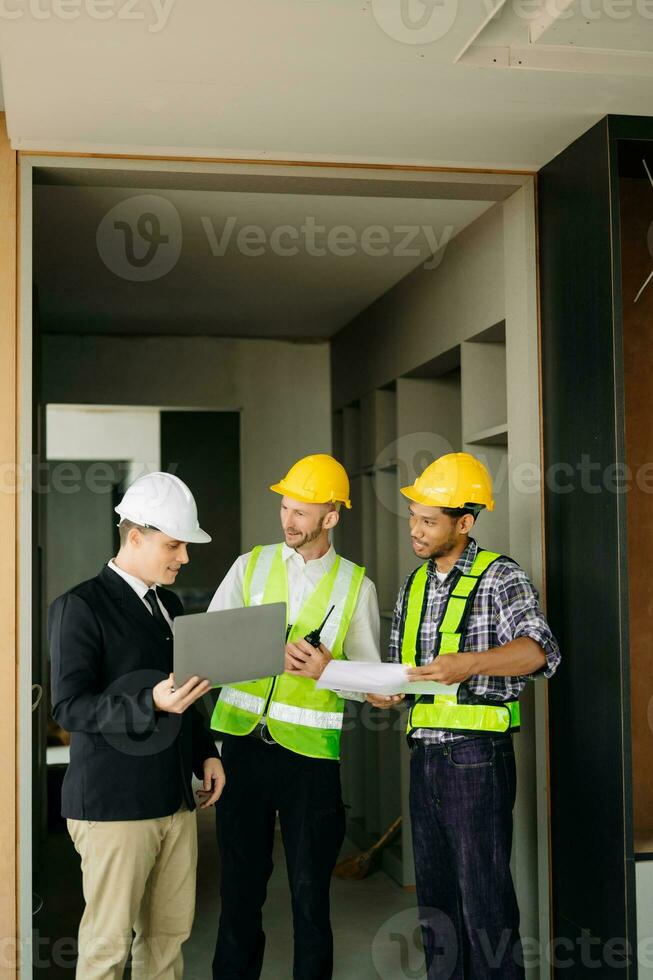 Contractor and architect looking at plan, tablet, laptop and talking about working on big project. Building in construction process photo