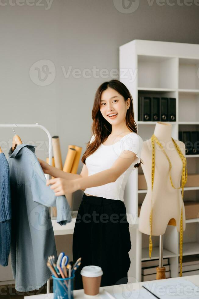 Asian tailor woman working on clothes in tailoring atelier.  beautiful young female fashion designer smile and after success in modern studio photo