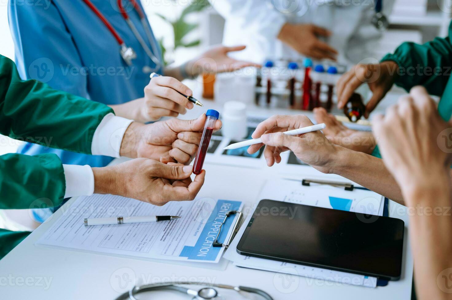 Medical team having a meeting with doctors in white lab coats and surgical scrubs seated at a table discussing a patients working online using computers photo