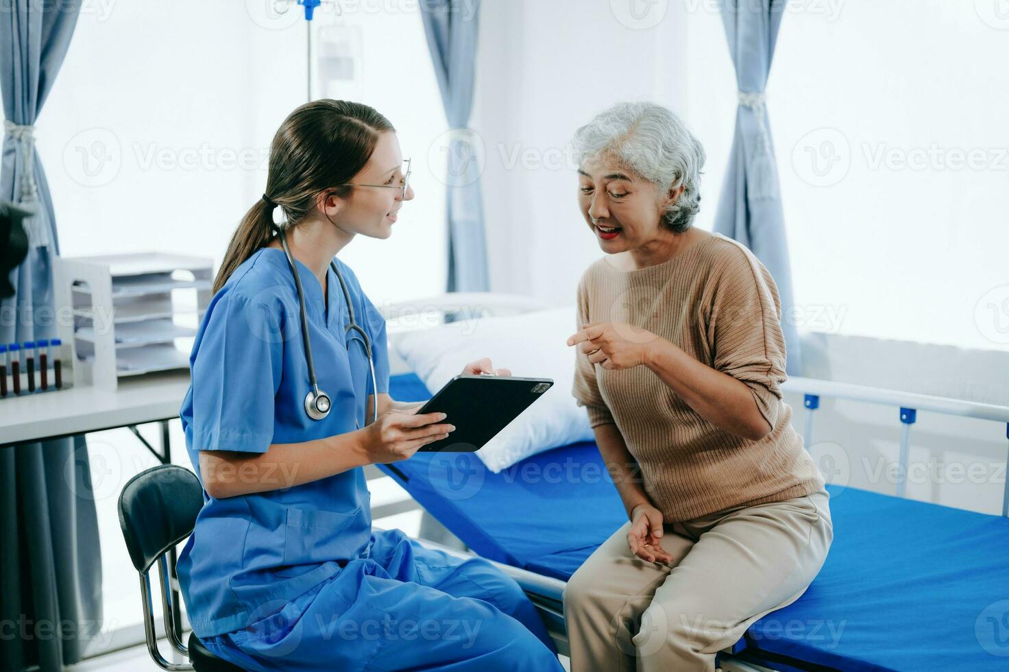 Friendly Female Head Nurse Making Rounds does Checkup on Patient Resting in Bed. She Checks tablet while Man Fully Recovering after Successful Surgery in hospital photo