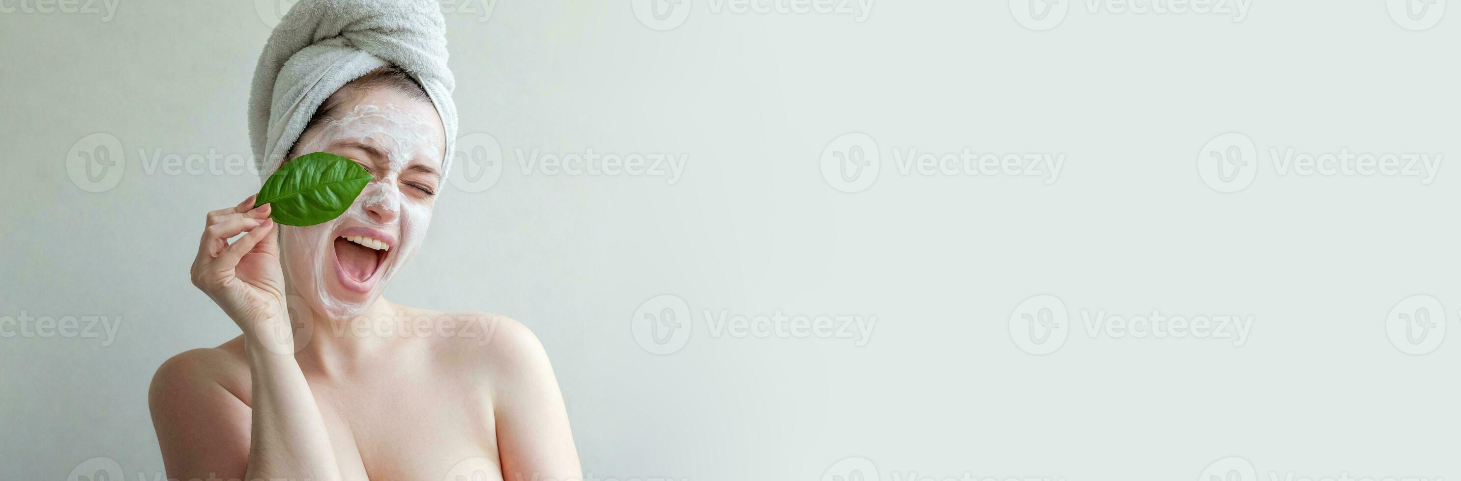 belleza retrato de mujer en toalla en cabeza con blanco nutritiva máscara o crema en cara y verde hoja en mano, blanco antecedentes aislado. protección de la piel limpieza eco orgánico cosmético spa concepto. foto