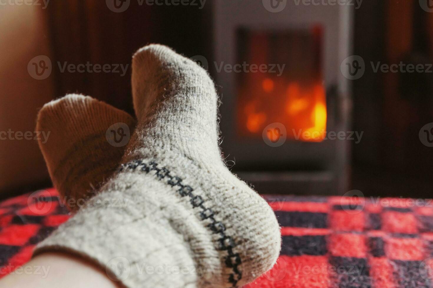Feet legs in winter clothes wool socks at fireplace background. Woman sitting at home on winter or autumn evening relaxing and warming up. Winter and cold weather concept. Hygge Christmas eve. photo