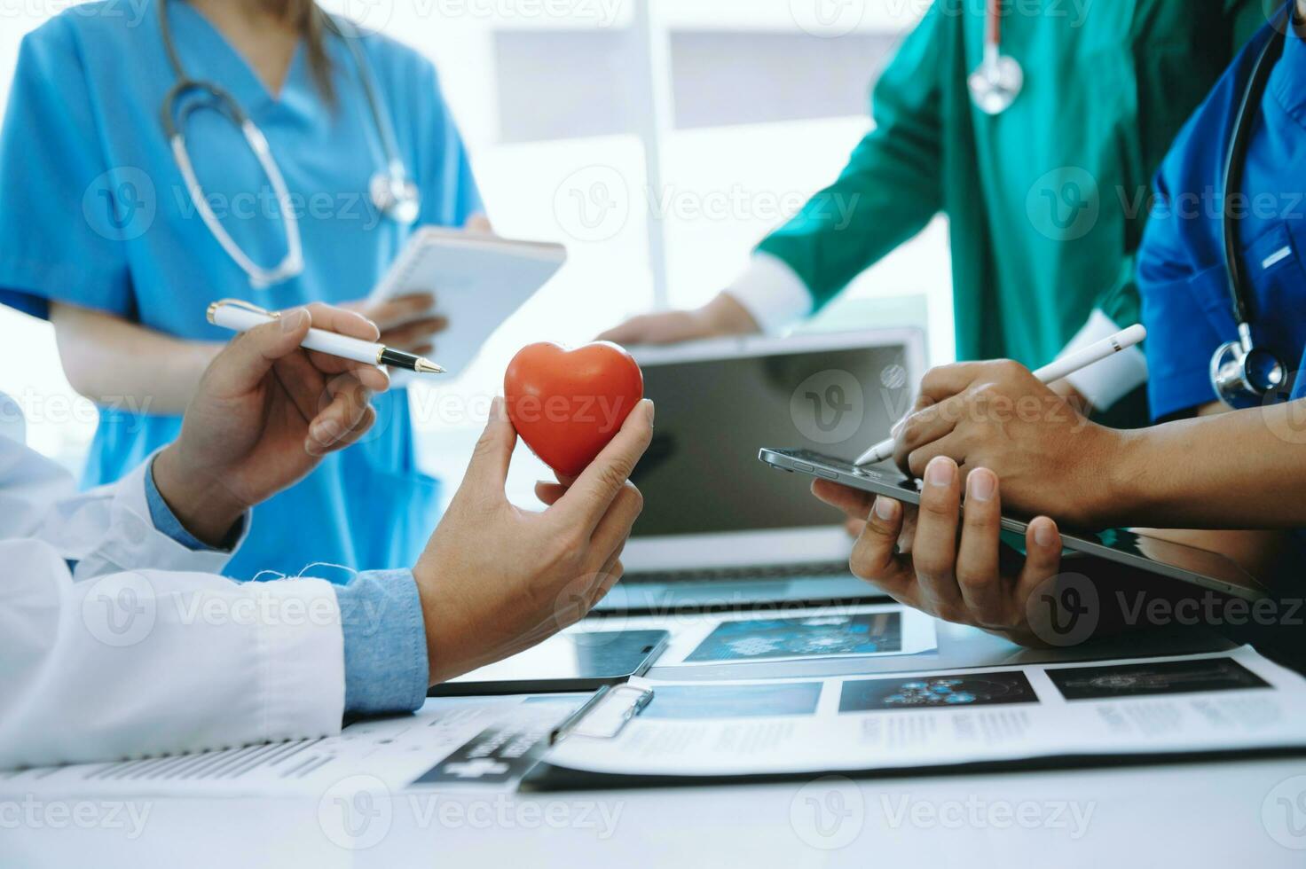 Medical team having a meeting with doctors in white lab coats and surgical scrubs seated at a table discussing a patients working online using computers in the medical industry photo