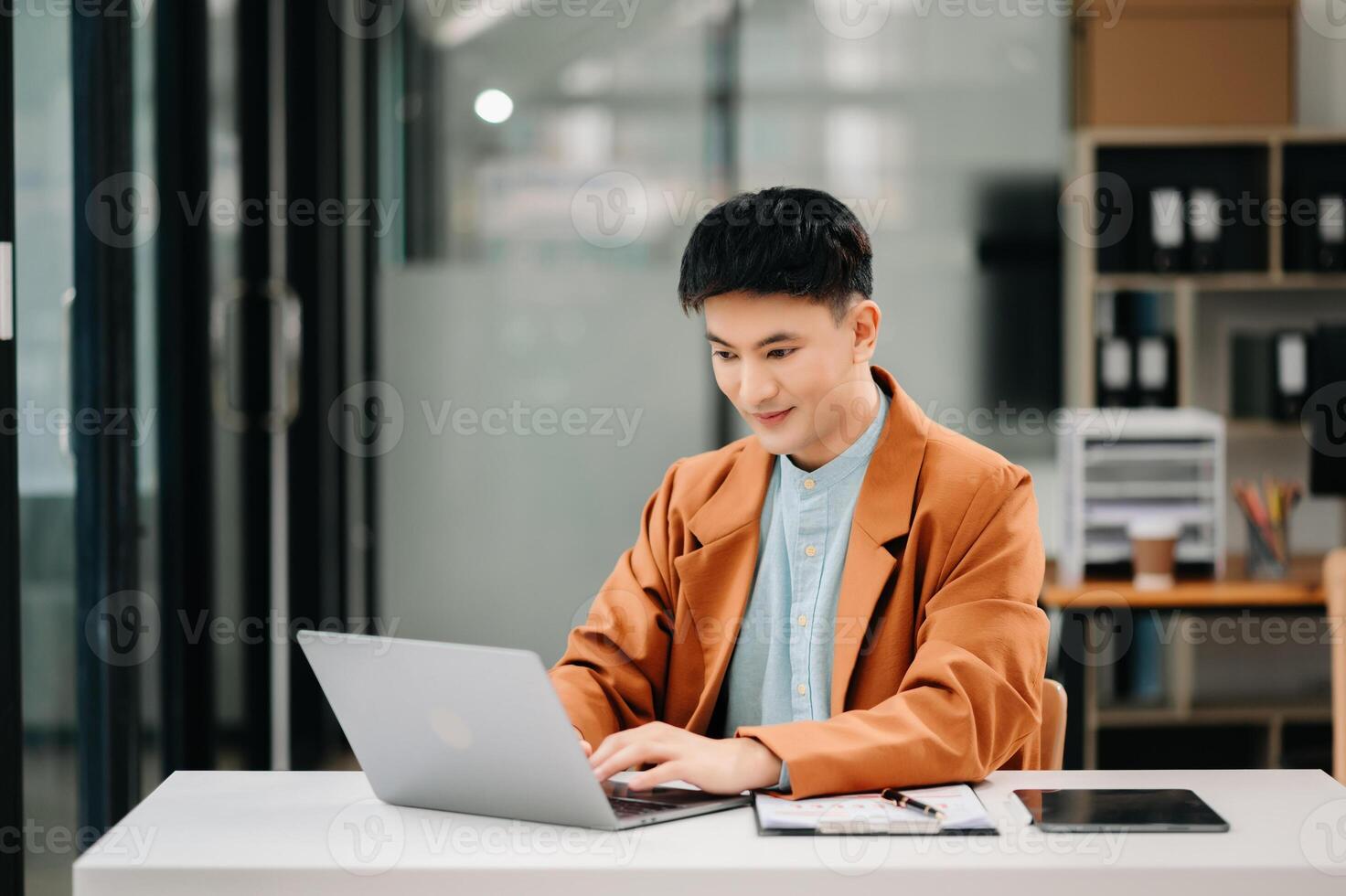 Business asian man Talking on the phone and using a laptop with a smile while sitting at modern office photo