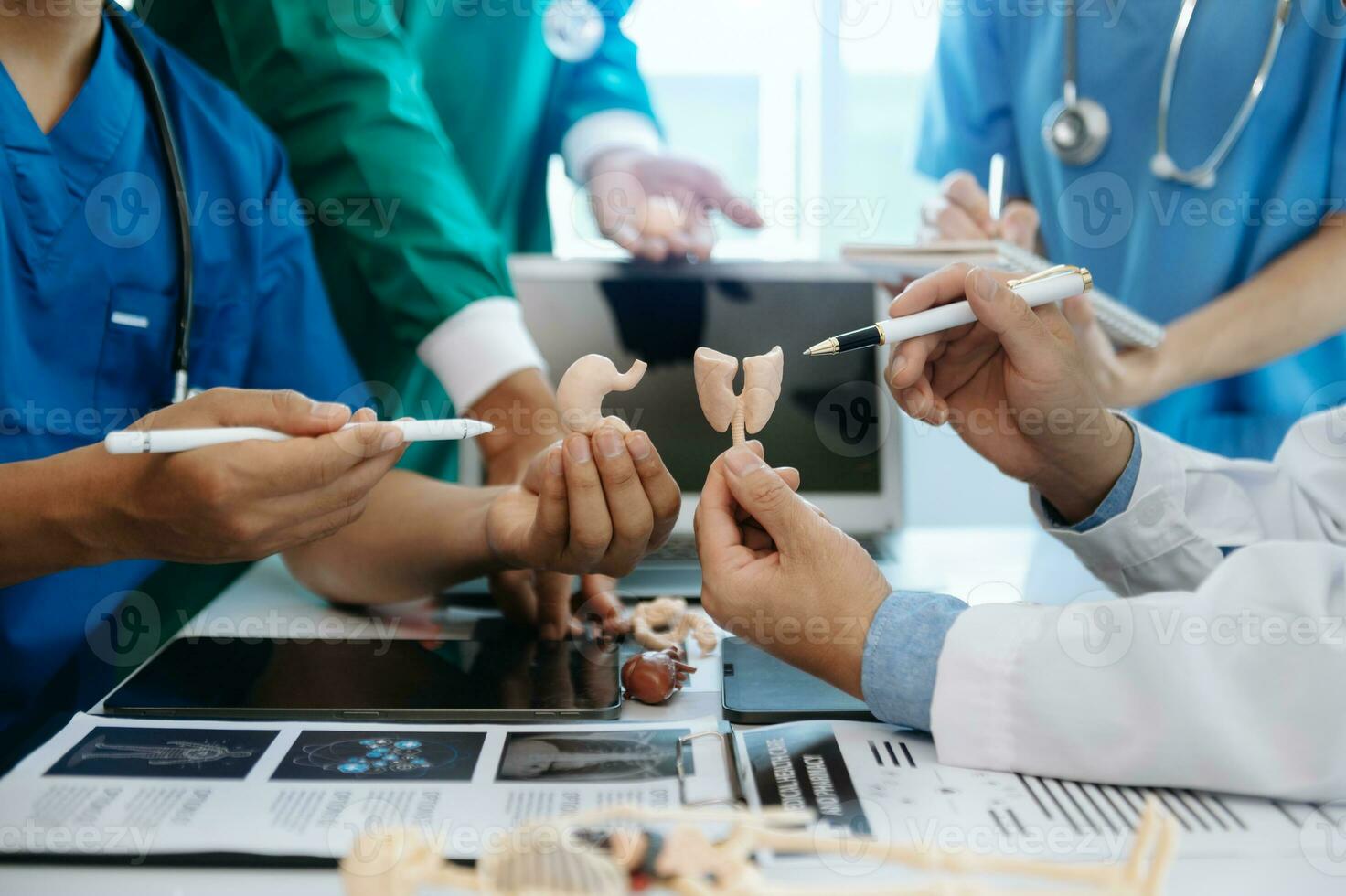 Medical team having a meeting with doctors in white lab coats and surgical scrubs seated at a table discussing a patients working online using computers in the medical industry photo