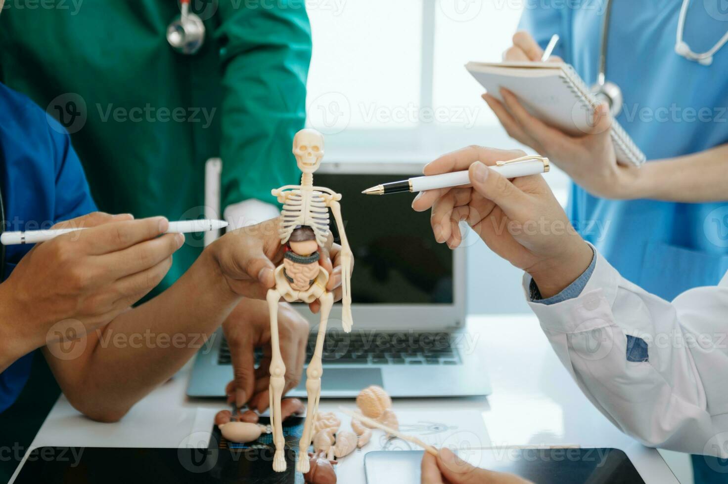 Medical team having a meeting with doctors in white lab coats and surgical scrubs seated at a table discussing a patients working online using computers in the medical industry photo