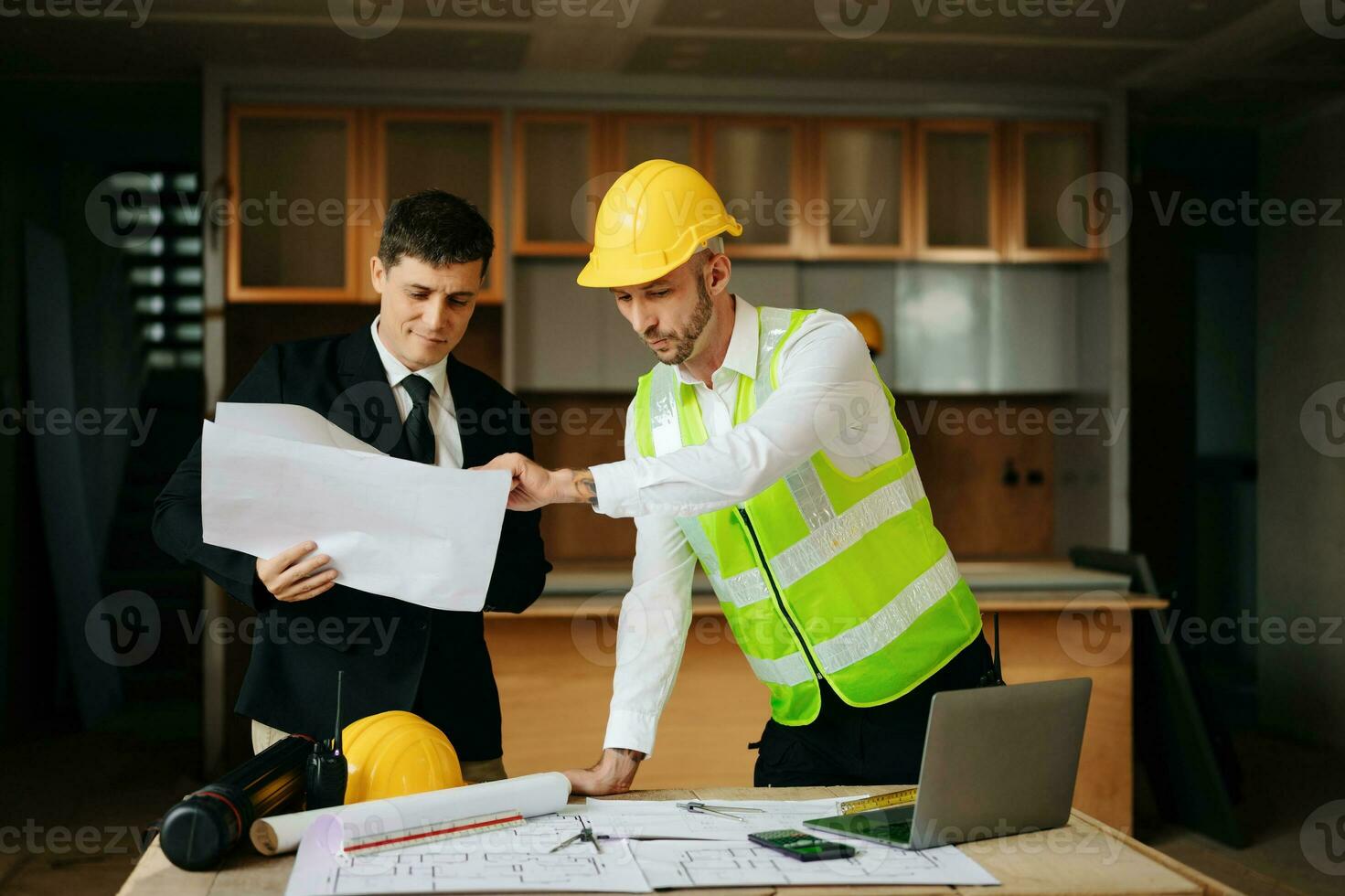 Contractor and architect looking at plan, tablet, laptop and talking about working on big project. Building in construction interior. photo