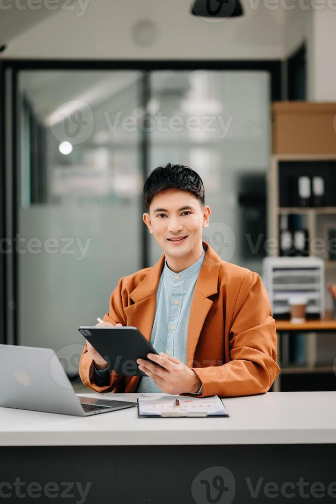 Business asian man Talking on the phone and using a laptop with a smile while sitting at modern office photo