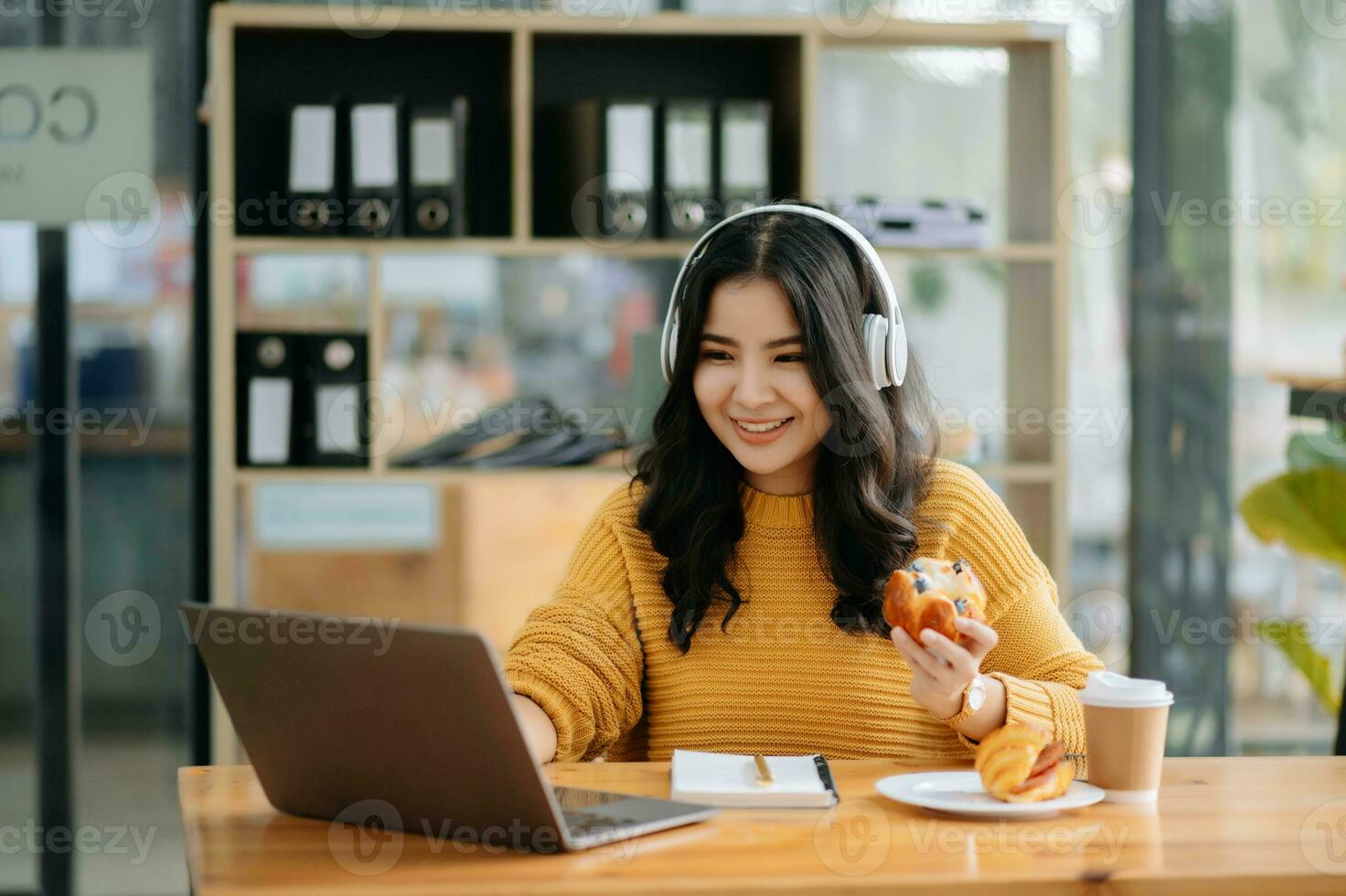 Attractive happy young Asian student studying at the college library, sitting at desk, using a laptop computer, tablet and headphones having a video chat. photo