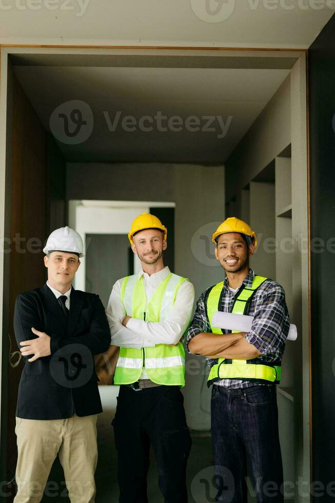 arquitecto caucásico hombre trabajando con colegas mezclado carrera en el construcción sitio. arquitectura Ingenieria en grande proyecto. edificio en construcción proceso interior. Mira a cámara foto