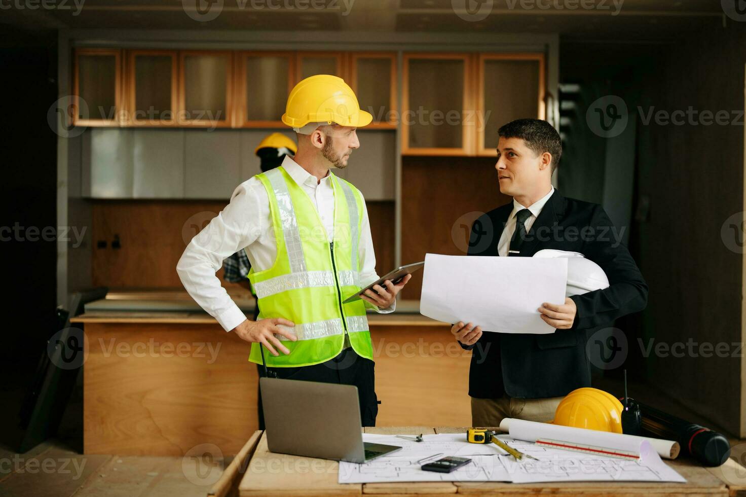 Contractor and architect looking at plan, tablet, laptop and talking about working on big project. Building in construction interior. photo