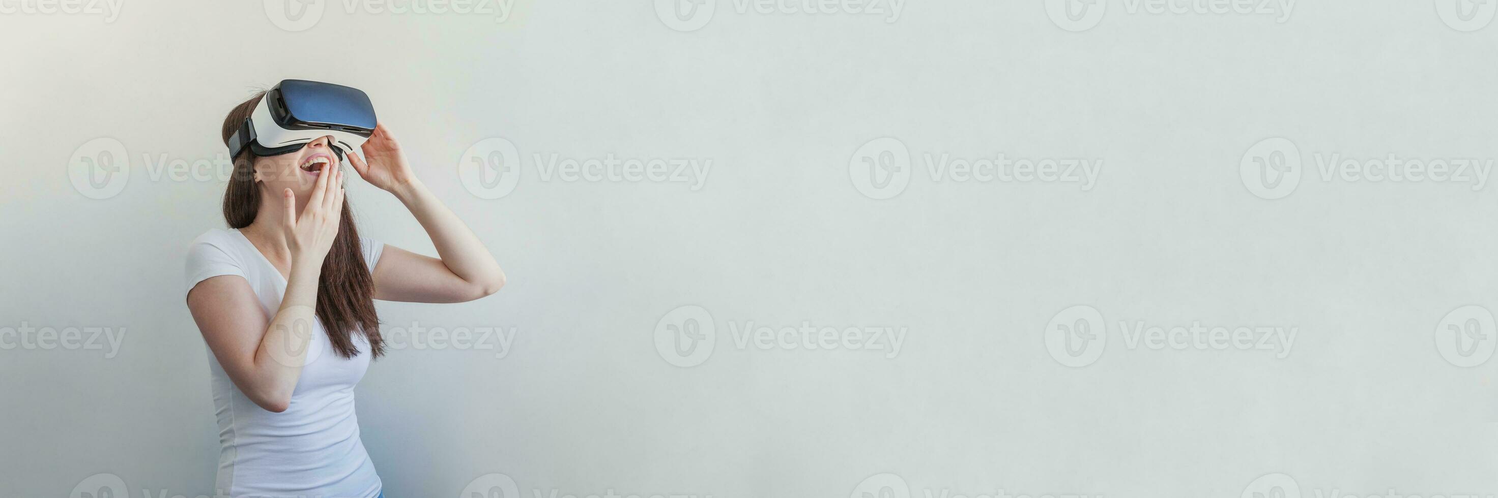 Smile young woman wearing using virtual reality VR glasses helmet headset on white background. Smartphone using with virtual reality goggles. Technology, simulation, hi-tech, videogame concept. Banner photo