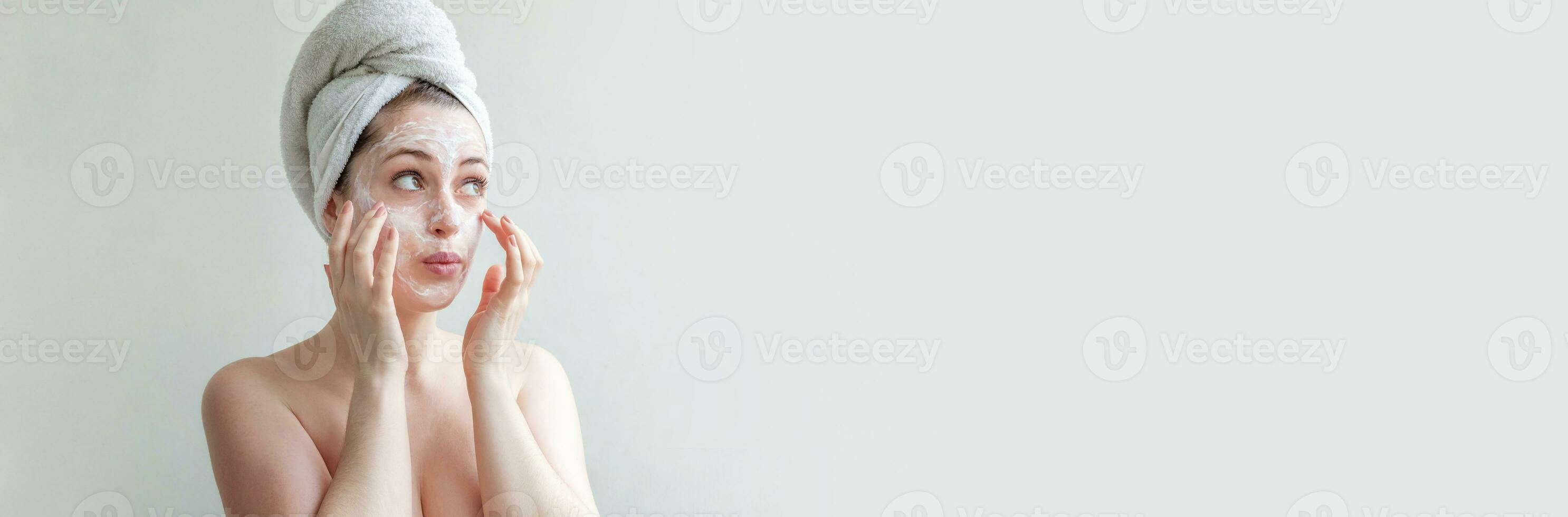 Beauty portrait of woman in towel on head with white nourishing mask or creme on face, white background isolated. Skincare cleansing eco organic cosmetic spa relax concept. Banner. photo