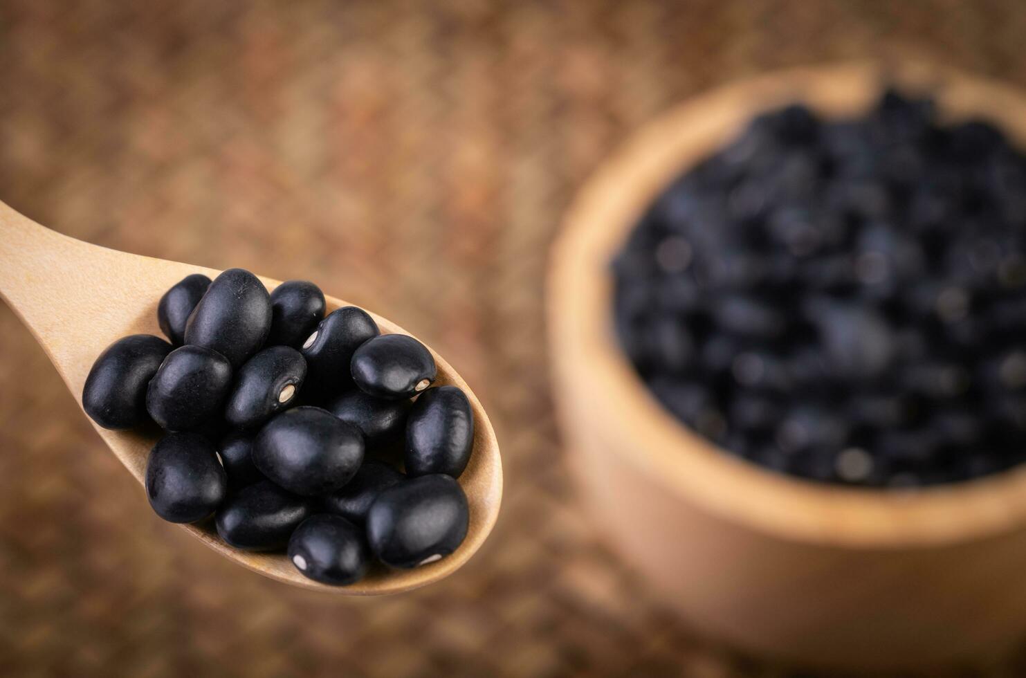 Black beans in a wooden spoon with Black beans in a wooden cup placed on a bamboo weave. photo