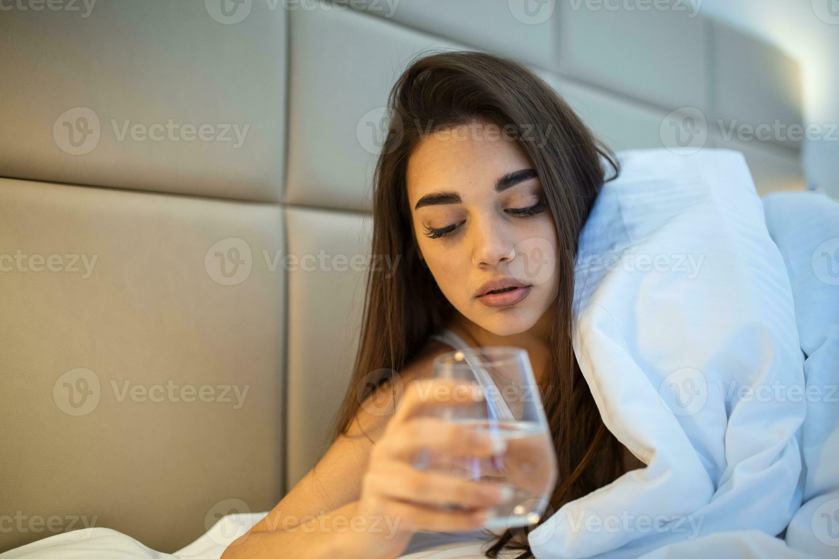 Young woman drinking glass of water in bed at night. Woman drinking a
