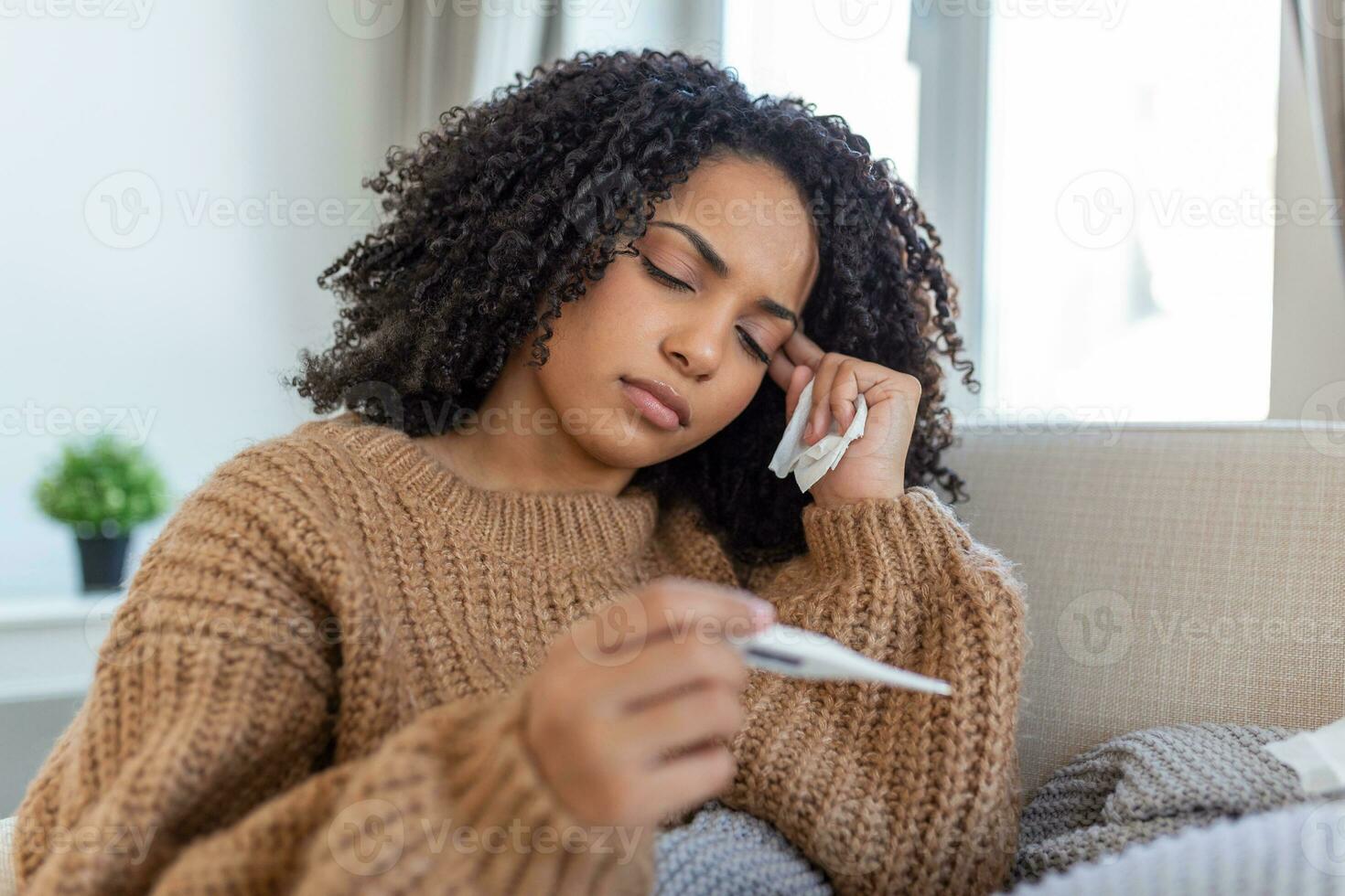 Woman is having flu and she is using thermometer. Sick with a rhinitis woman dripping nose. Woman being sick having flu lying on sofa looking at temperature on thermometer. photo