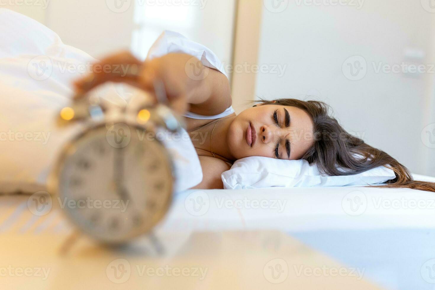 mujer acostado en cama torneado apagado un alarma reloj en el Mañana a 5 de la mañana. mano vueltas apagado el alarma reloj despertar arriba a mañana, niña vueltas apagado el alarma reloj despertar arriba en el Mañana desde un llamar. foto