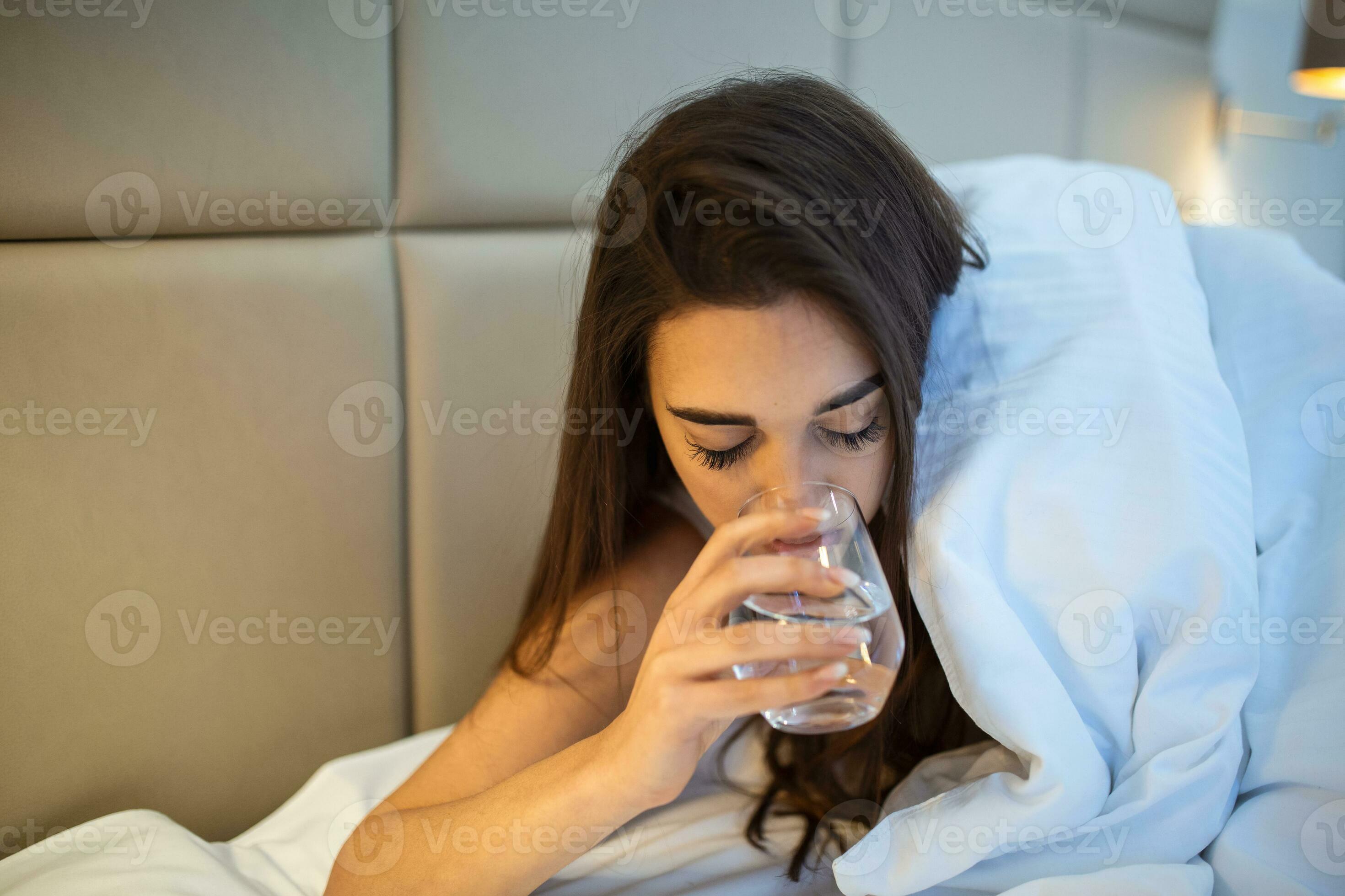 Young woman drinking glass of water in bed at night. Woman drinking a