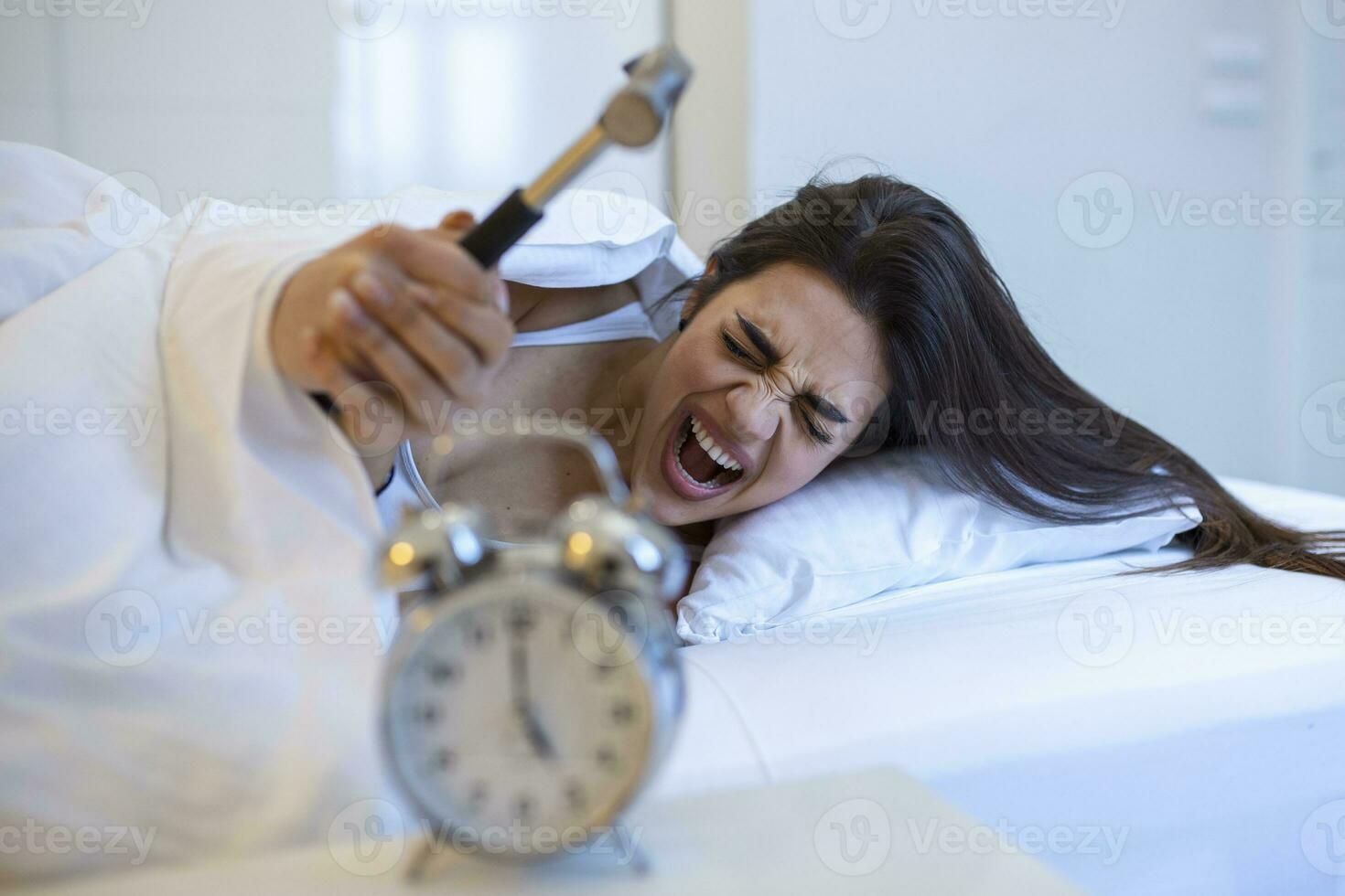 Young woman tries to break the alarm clock with hammer, Destroy the Clock. Girl lying in bed turning off an alarm clock with hammer in the morning at 5am. photo