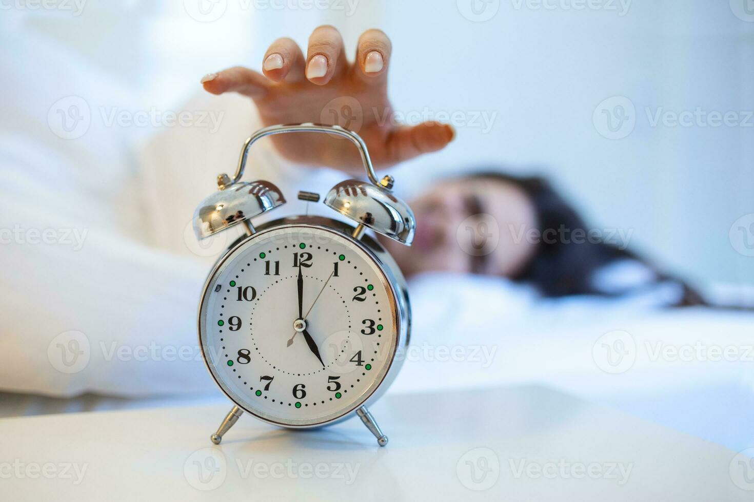 Woman lying in bed turning off an alarm clock in the morning at 5am. Hand turns off the alarm clock waking up at morning, girl turns off the alarm clock waking up in the morning from a call. photo