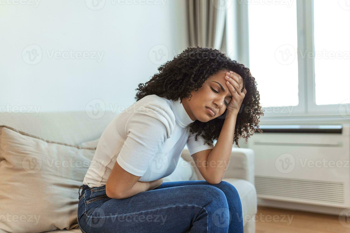 Woman in painful expression holding hands against belly suffering menstrual period pain, lying sad on home bed, having tummy cramp in female health concept photo