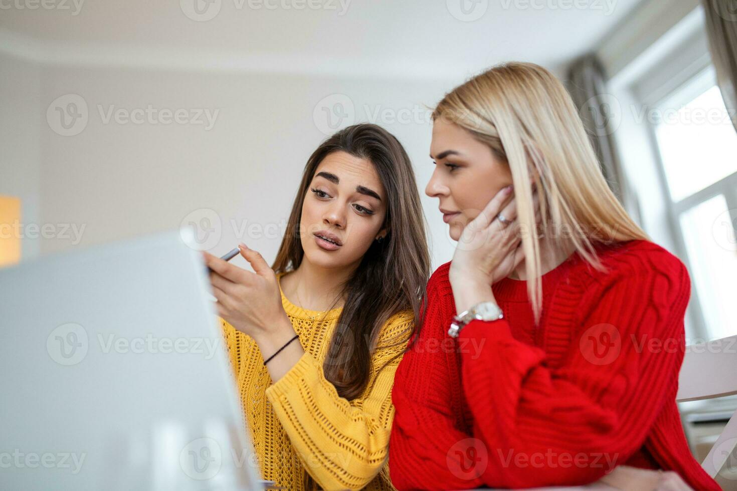 Clever female students discussing ideas for coursework project reading information from network on laptop computer,young women watching tutorial together having conversation in office photo