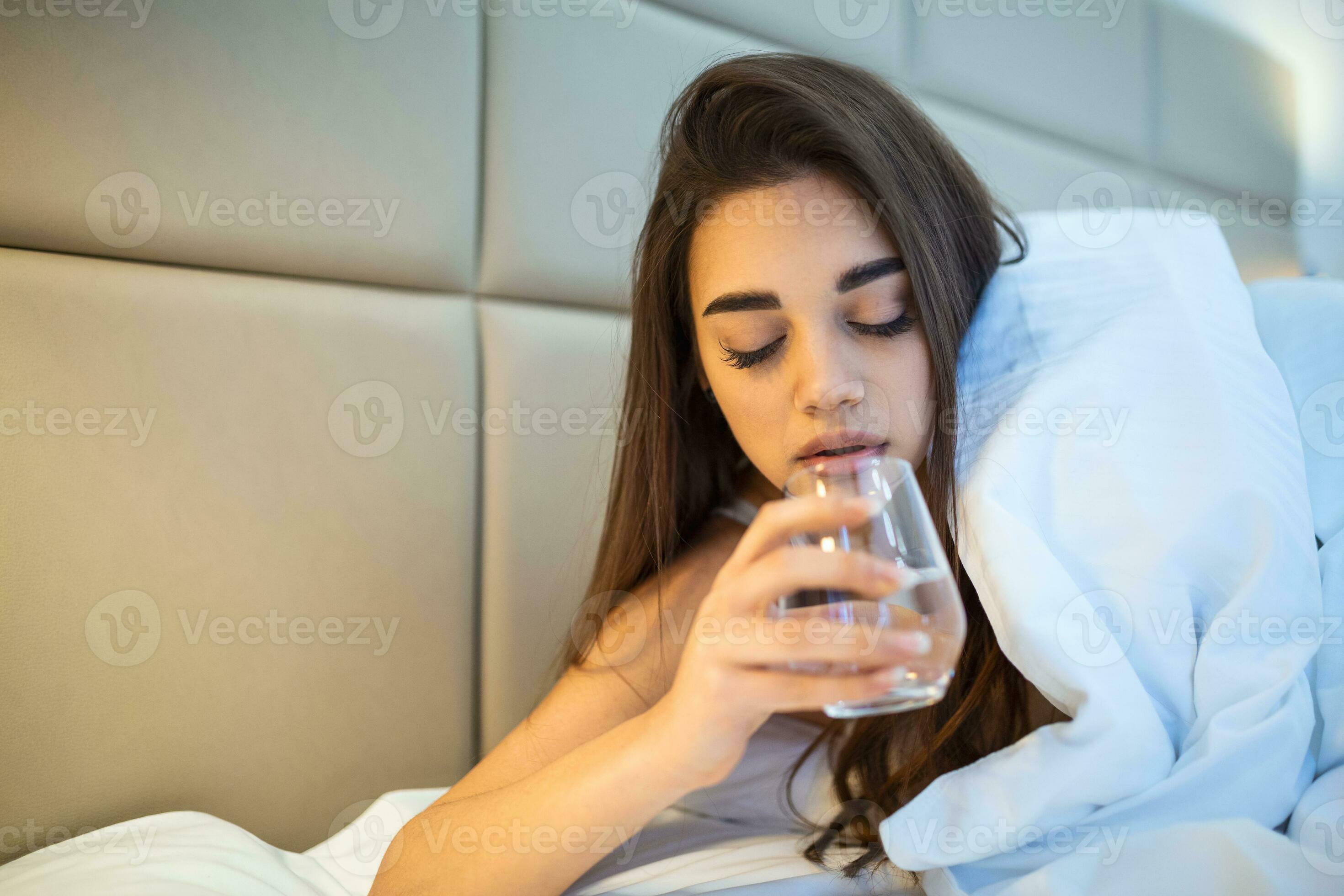 Young woman drinking glass of water in bed at night. Woman drinking a
