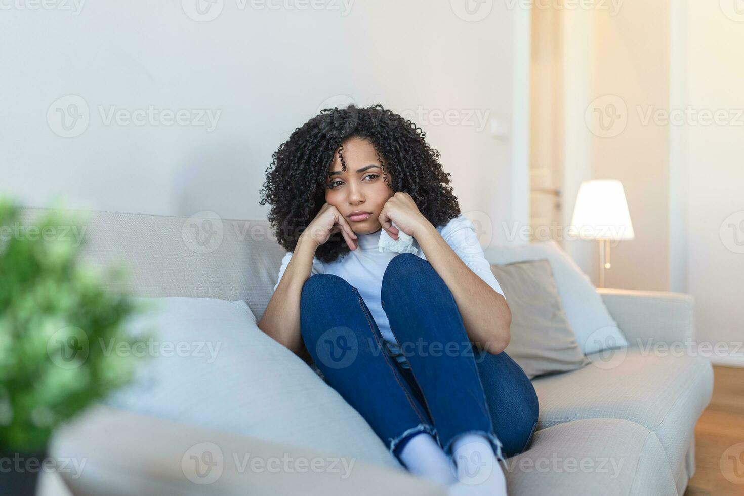 infeliz africano americano mujer en sofá llanto. solitario triste mujer profundo en pensamientos sentado soñador o esperando para alguien en el vivo habitación con un grave expresión, sentado en sofá foto