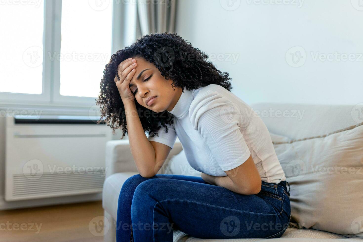 African American Woman in painful expression holding hands against belly suffering menstrual period pain, lying sad on home bed, having tummy cramp in female health concept photo