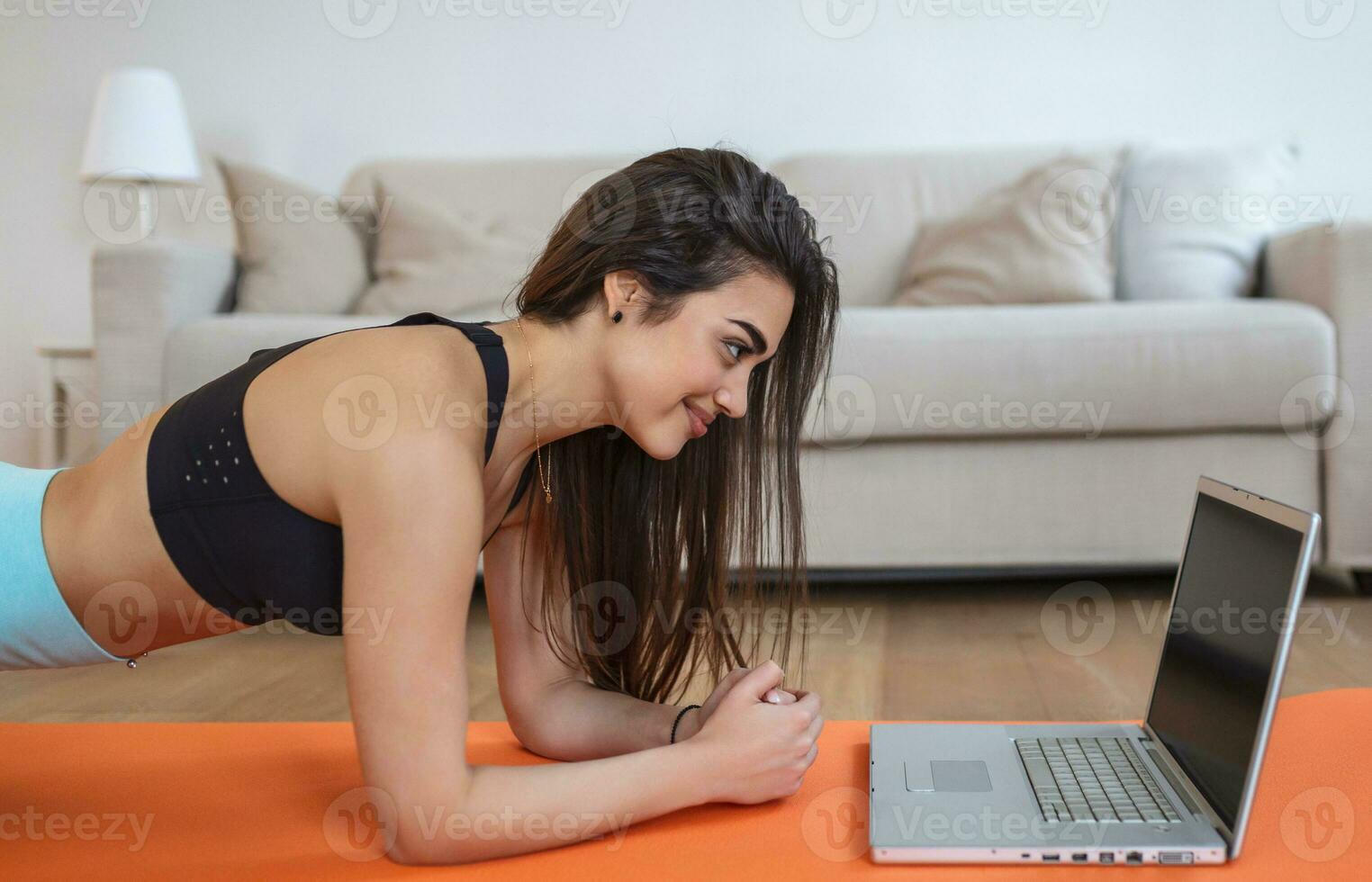 Portrait of young attractive woman doing exercises while watching online lessons on her laptop. Healthy lifestyle and sports concept. Shot of fitness woman sitting on exercise mat photo