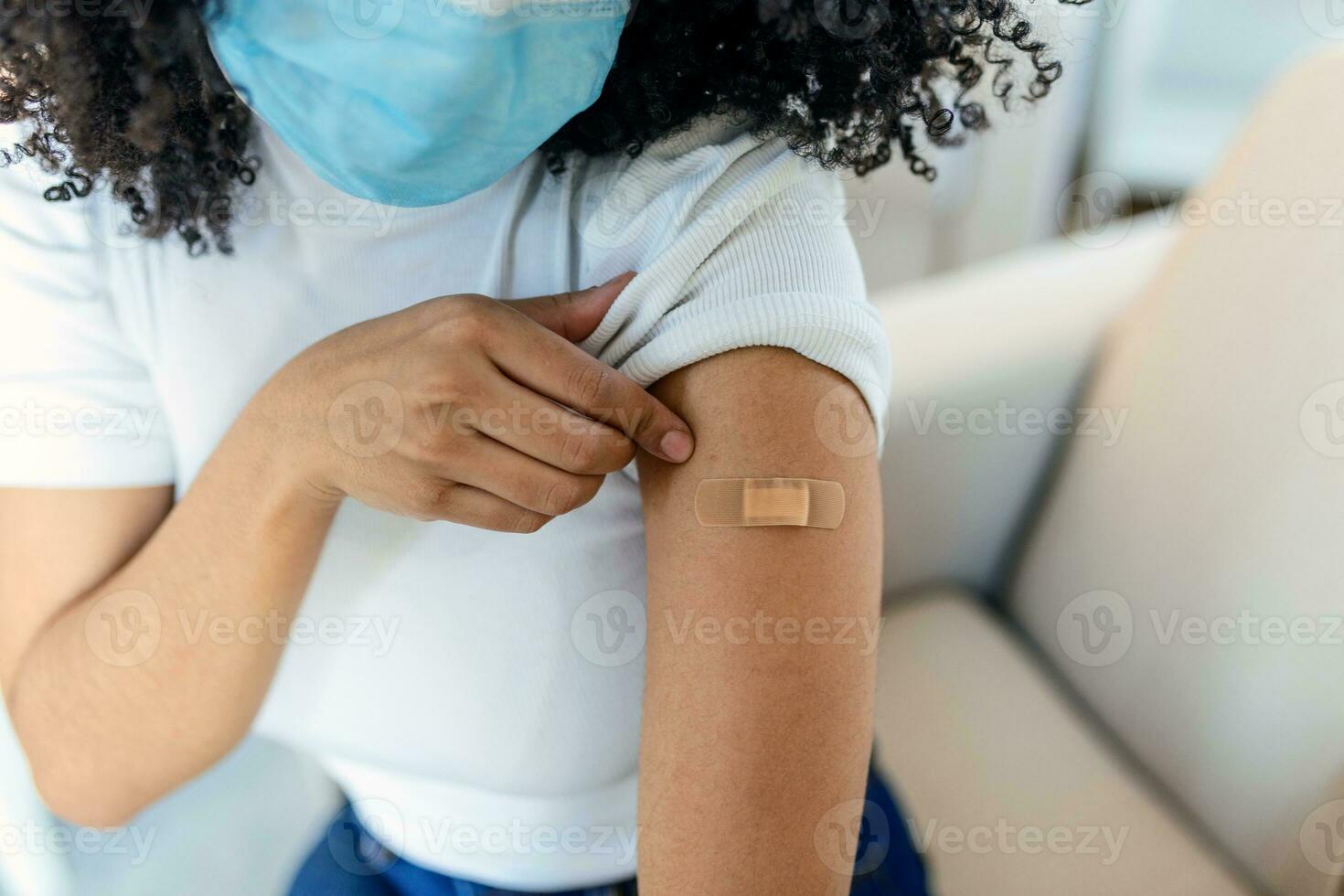 African woman holding up her shirt sleeve and showing her arm with bandage after receiving vaccination. covid 19 immunization photo