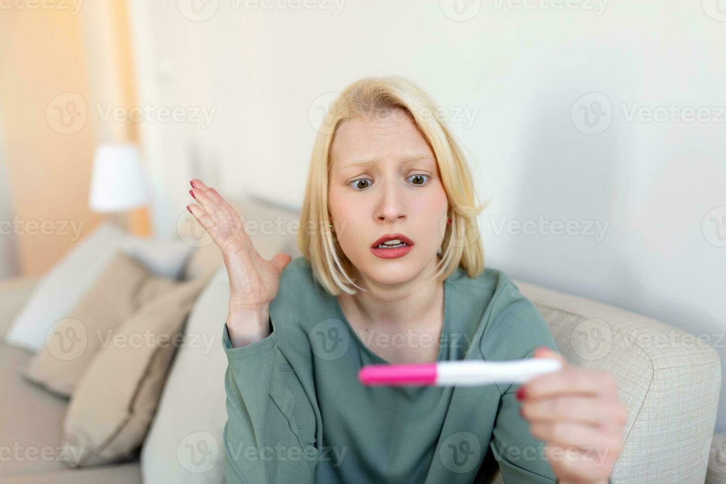 Sad, worried woman checking her recent pregnancy test, sitting on couch at home. Maternity, child birth and family problems concept. unwanted pregnancy photo