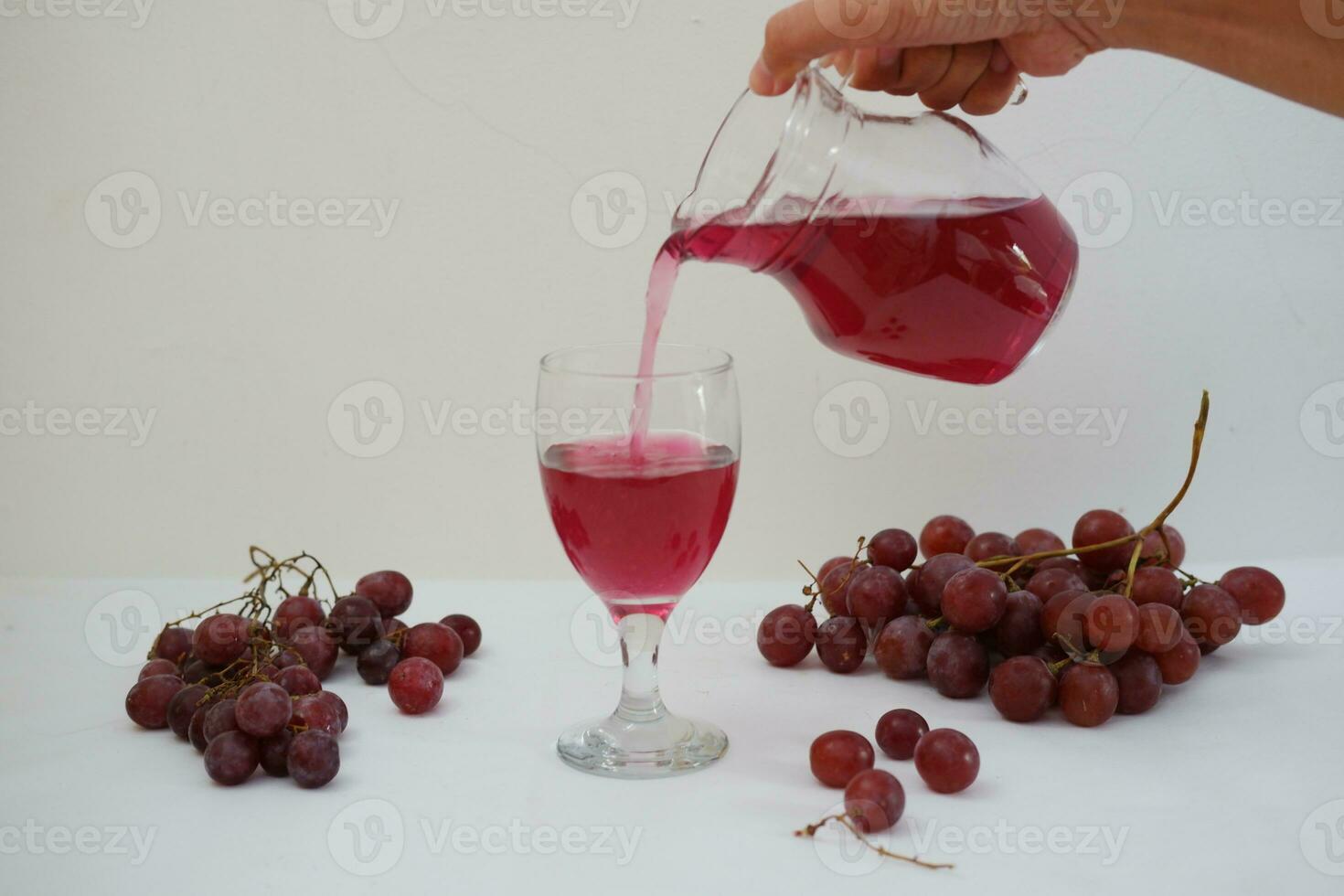 Red grape juice pouring into a glass with fresh grapes on white background photo
