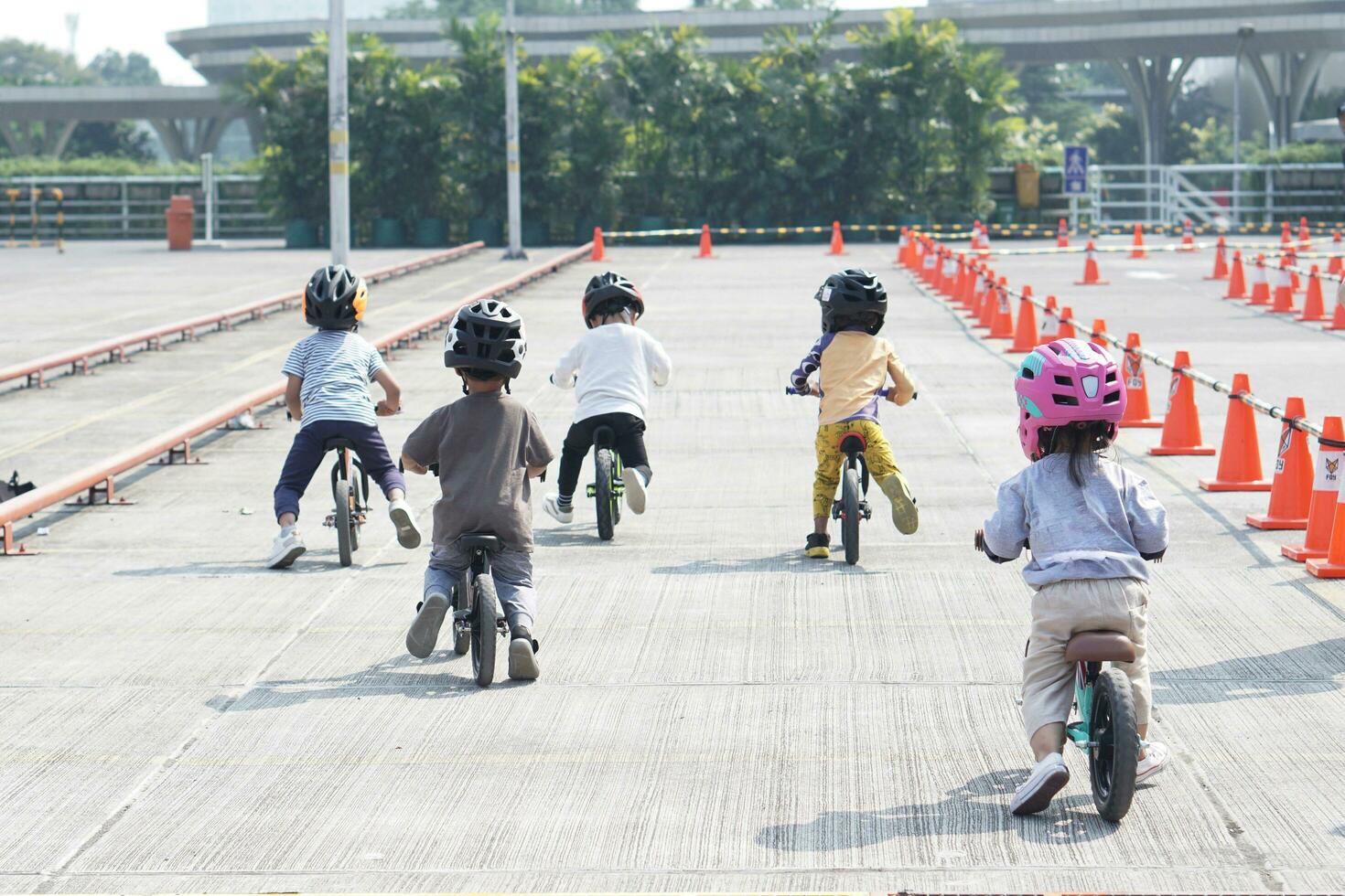 kids from 2-5 years old races on balance bike in a parking area with cones as track, back view, behind view shoot. photo