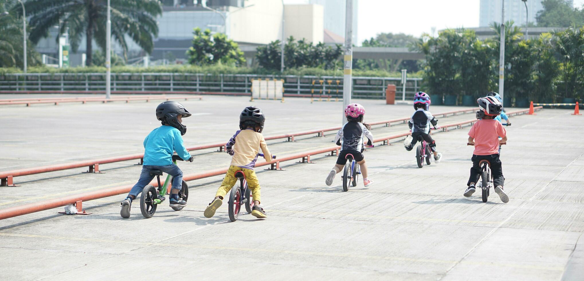 kids from 2-5 years old races on balance bike in a parking area with cones as track, back view, behind view shoot. photo