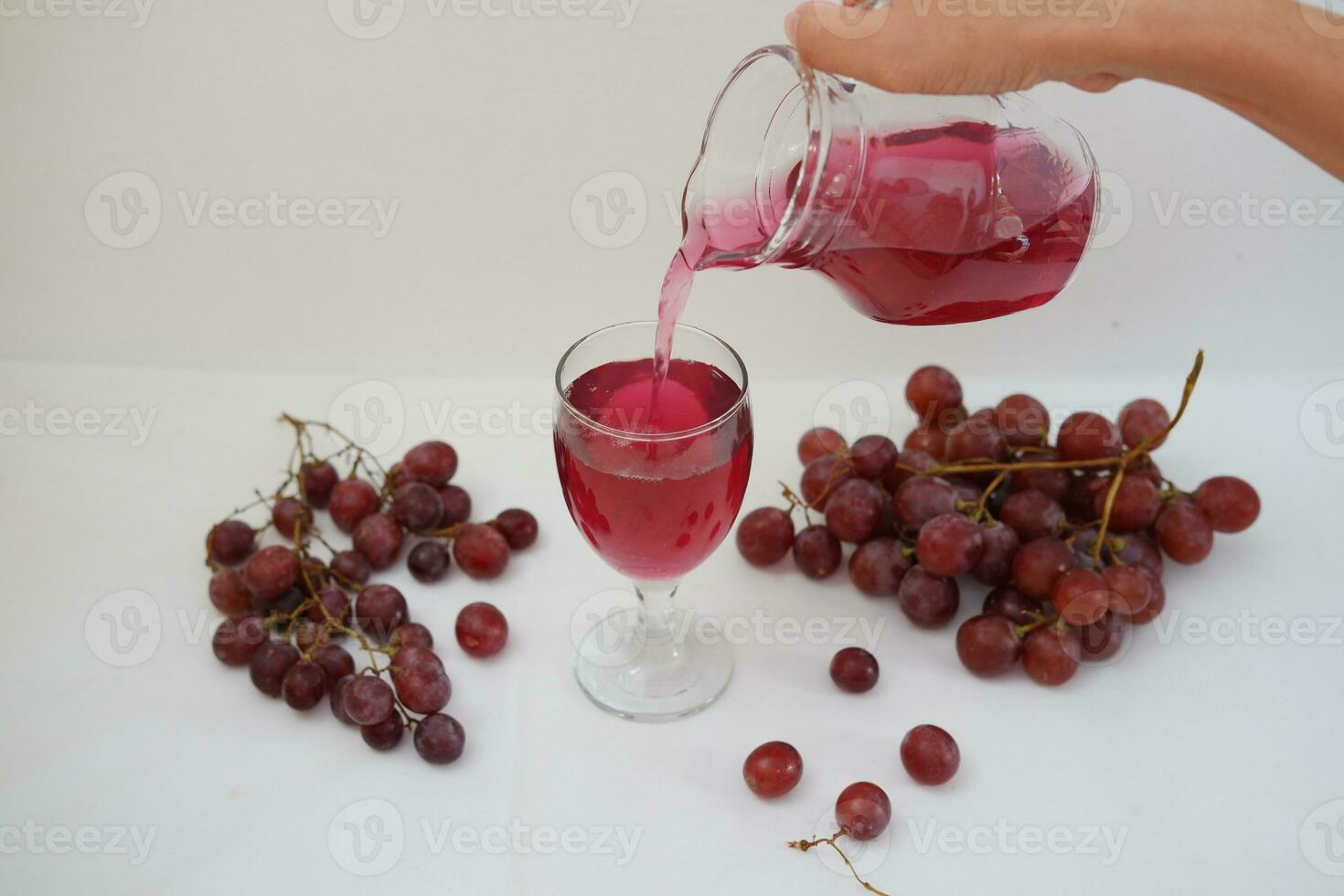 Red grape juice pouring into a glass with fresh grapes on white background photo