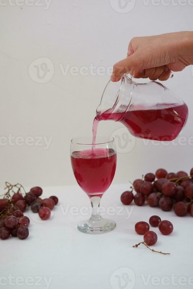 Red grape juice pouring into a glass with fresh grapes on white background photo
