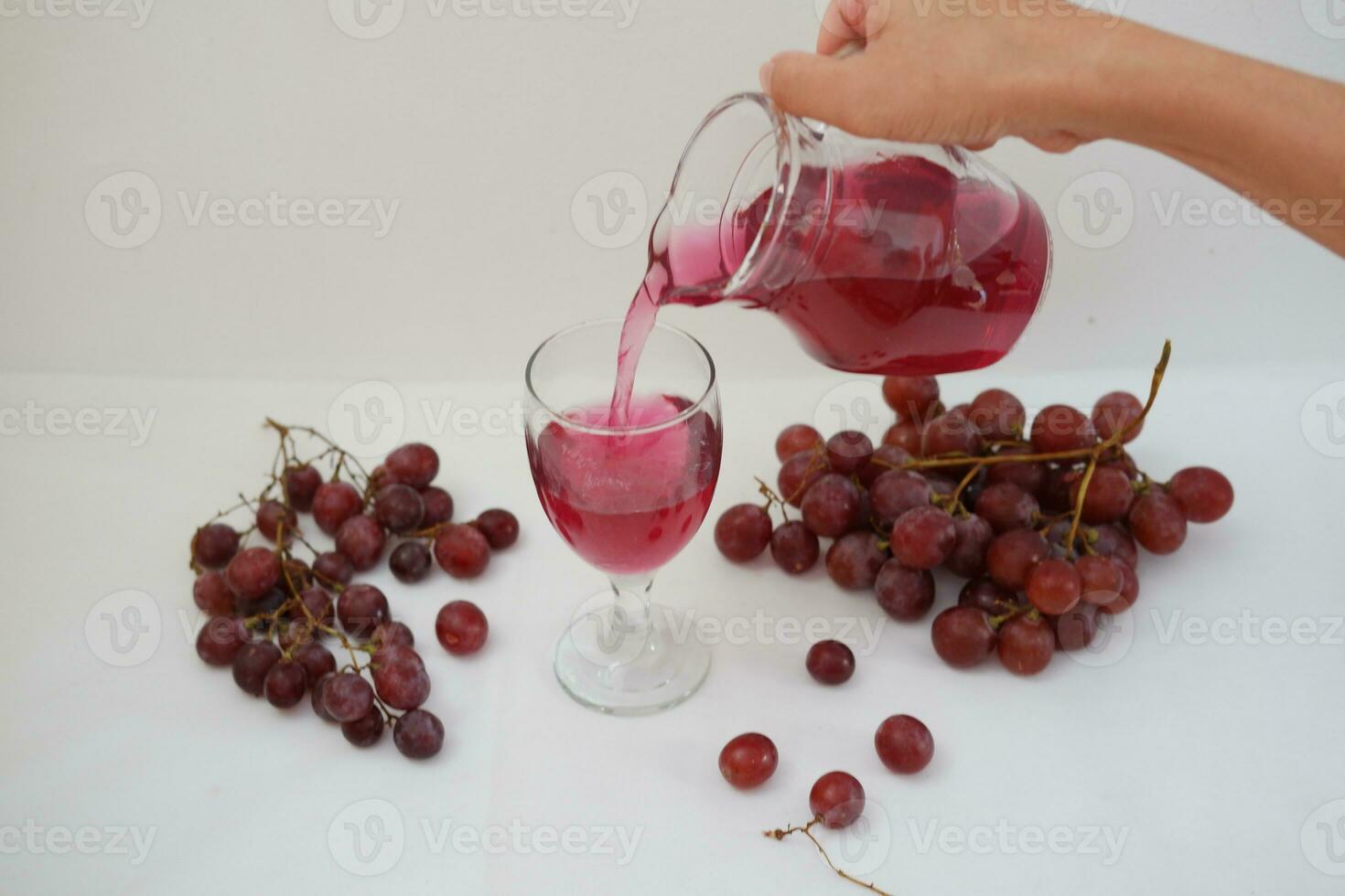 Red grape juice pouring into a glass with fresh grapes on white background photo