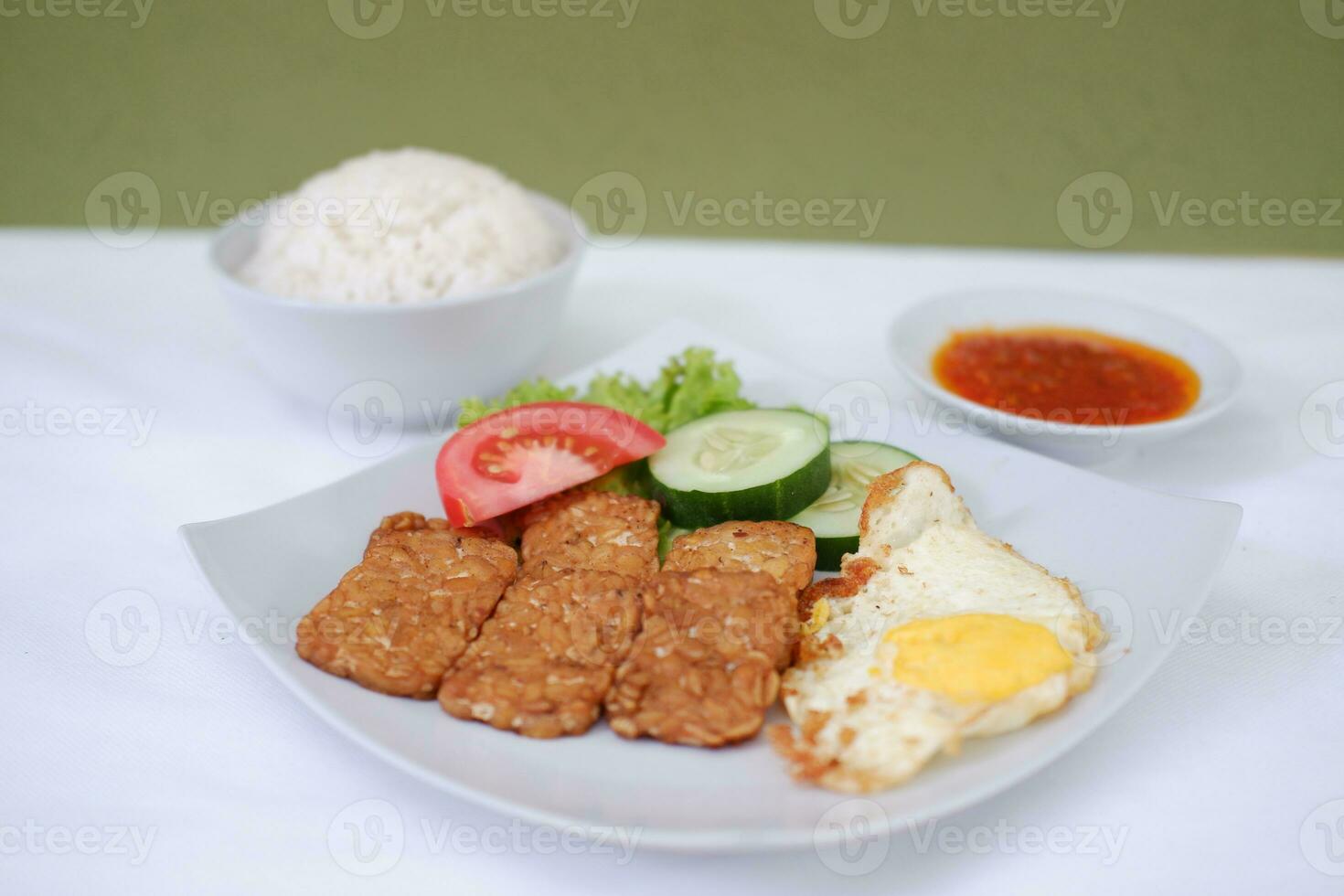 Fried tempeh cutlet with rice and fried egg on white plate photo