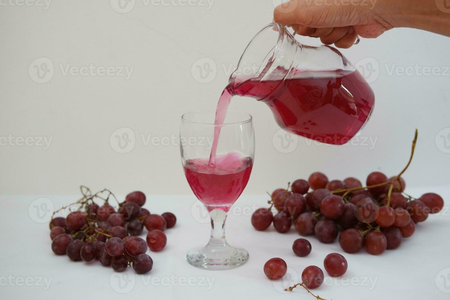 Red grape juice pouring into a glass with fresh grapes on white background photo