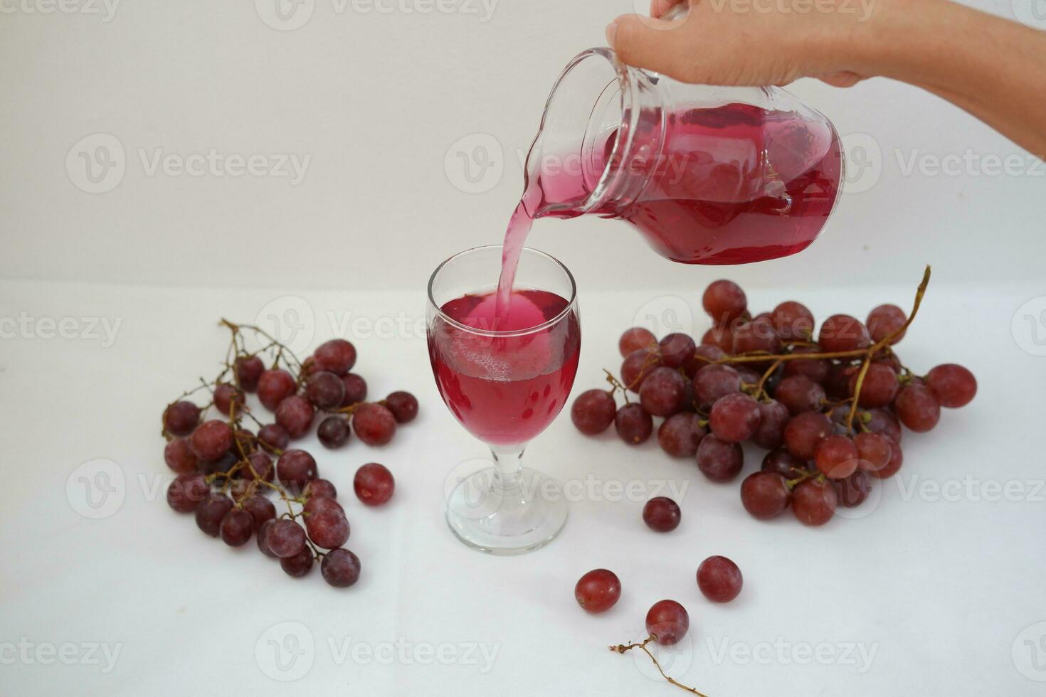 Red grape juice pouring into a glass with fresh grapes on white background photo